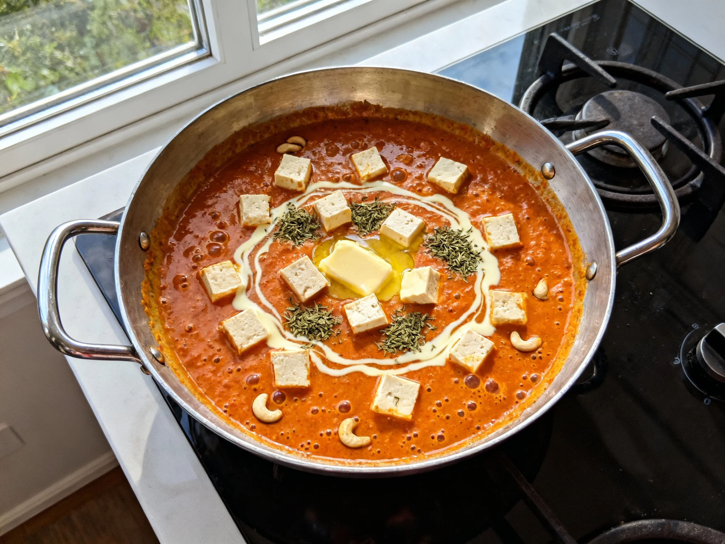Food photography, Overhead shot of butter paneer finishing in a wide skillet: silky orange-red tomato–cashew gravy gentl
