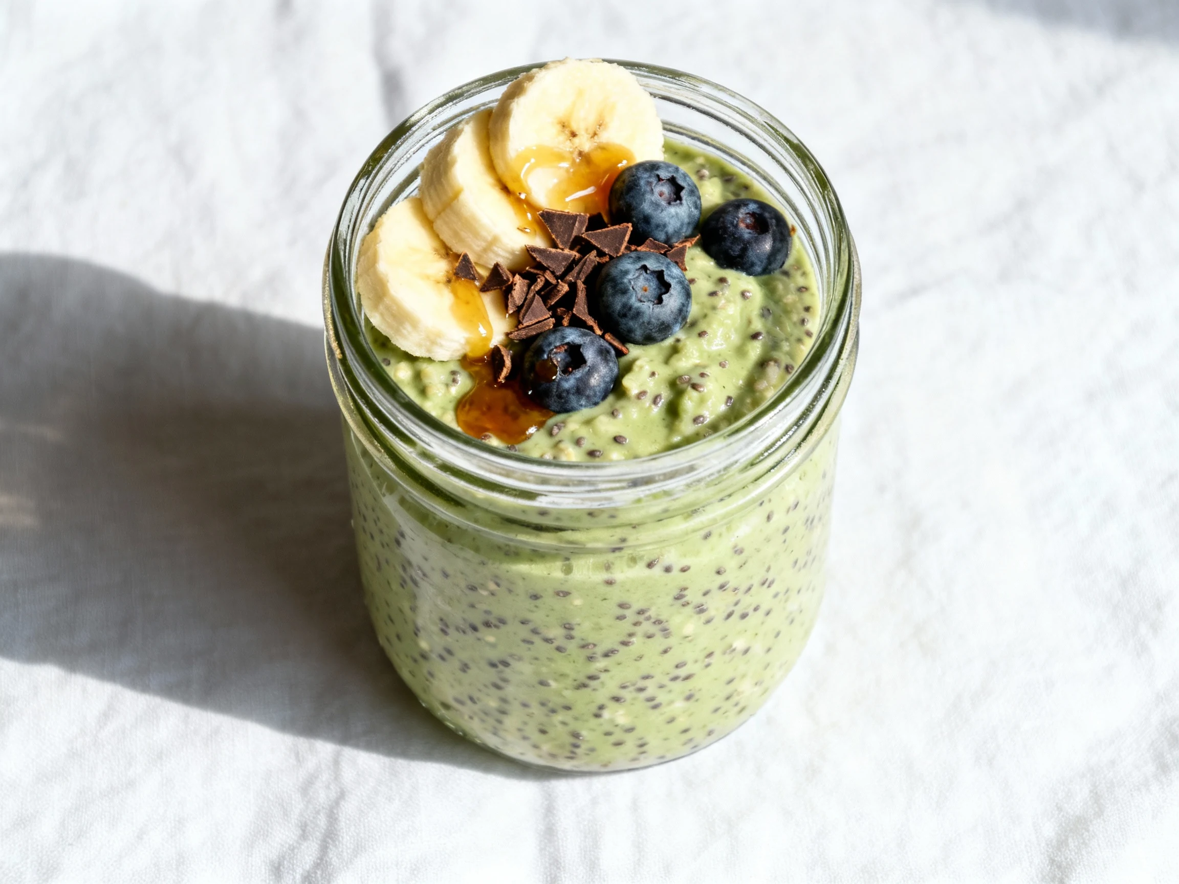 Food photography, 2. Overhead shot of matcha overnight oats in a glass jar, thick and creamy with chia, topped with bana