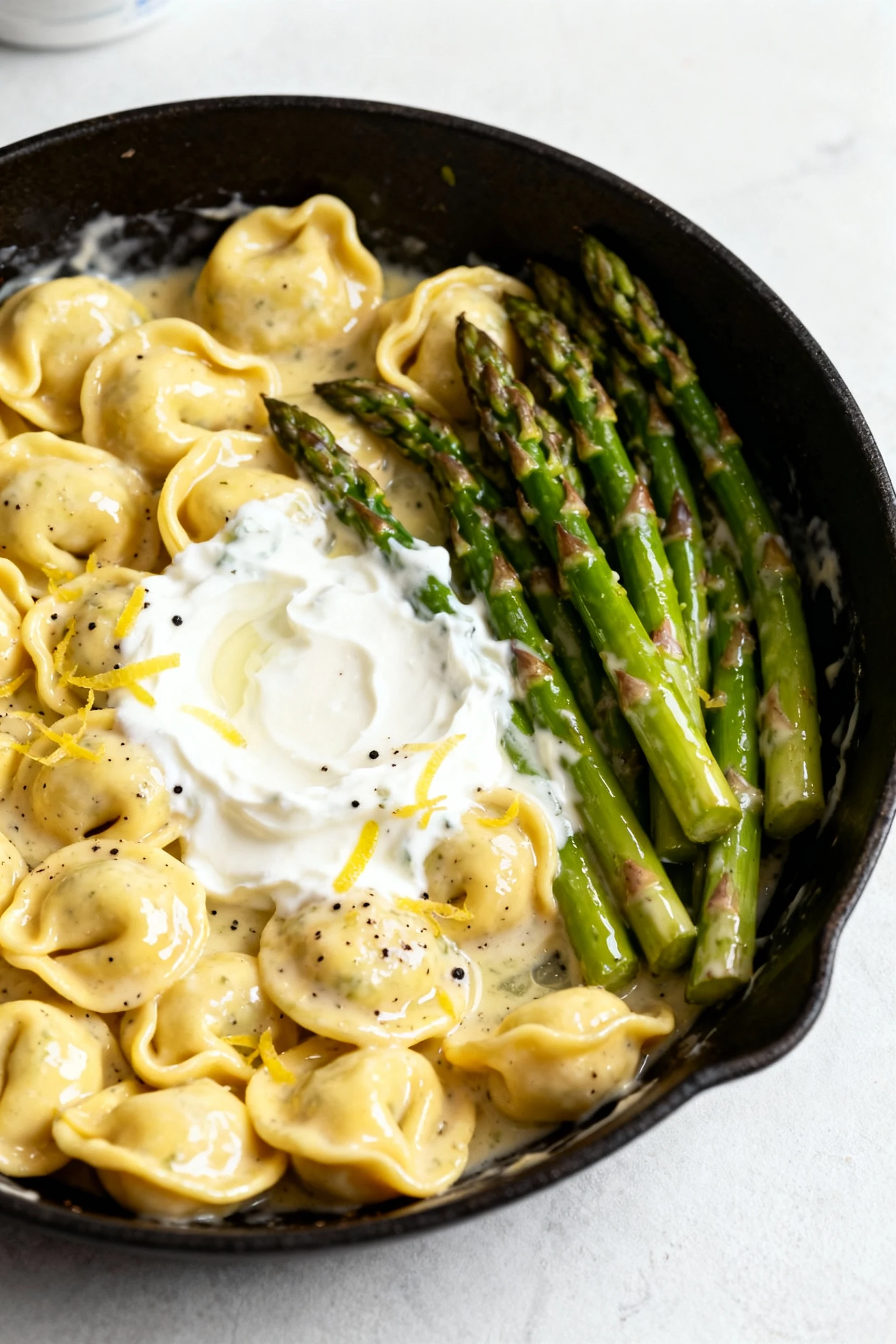 Food photography, Cooking process, 3/4 angle: skillet of cheese tortellini and crisp-tender asparagus being coated in a 