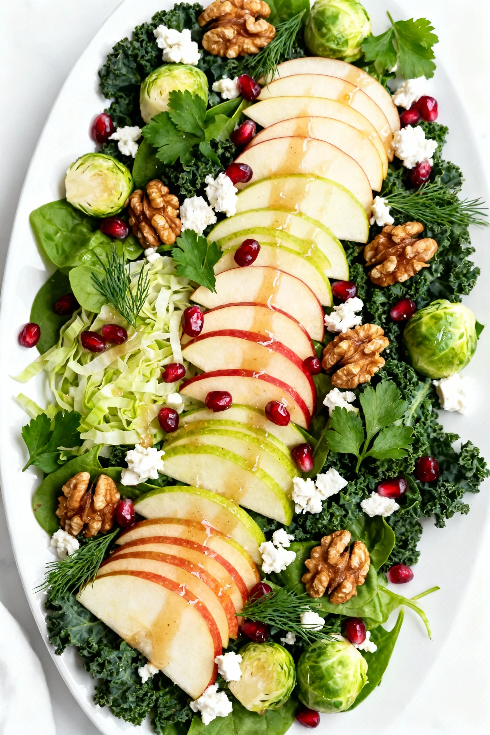 Overhead shot of the base festive salad on a wide white platter: mixed baby greens, massaged Tuscan kale, shaved Brussel