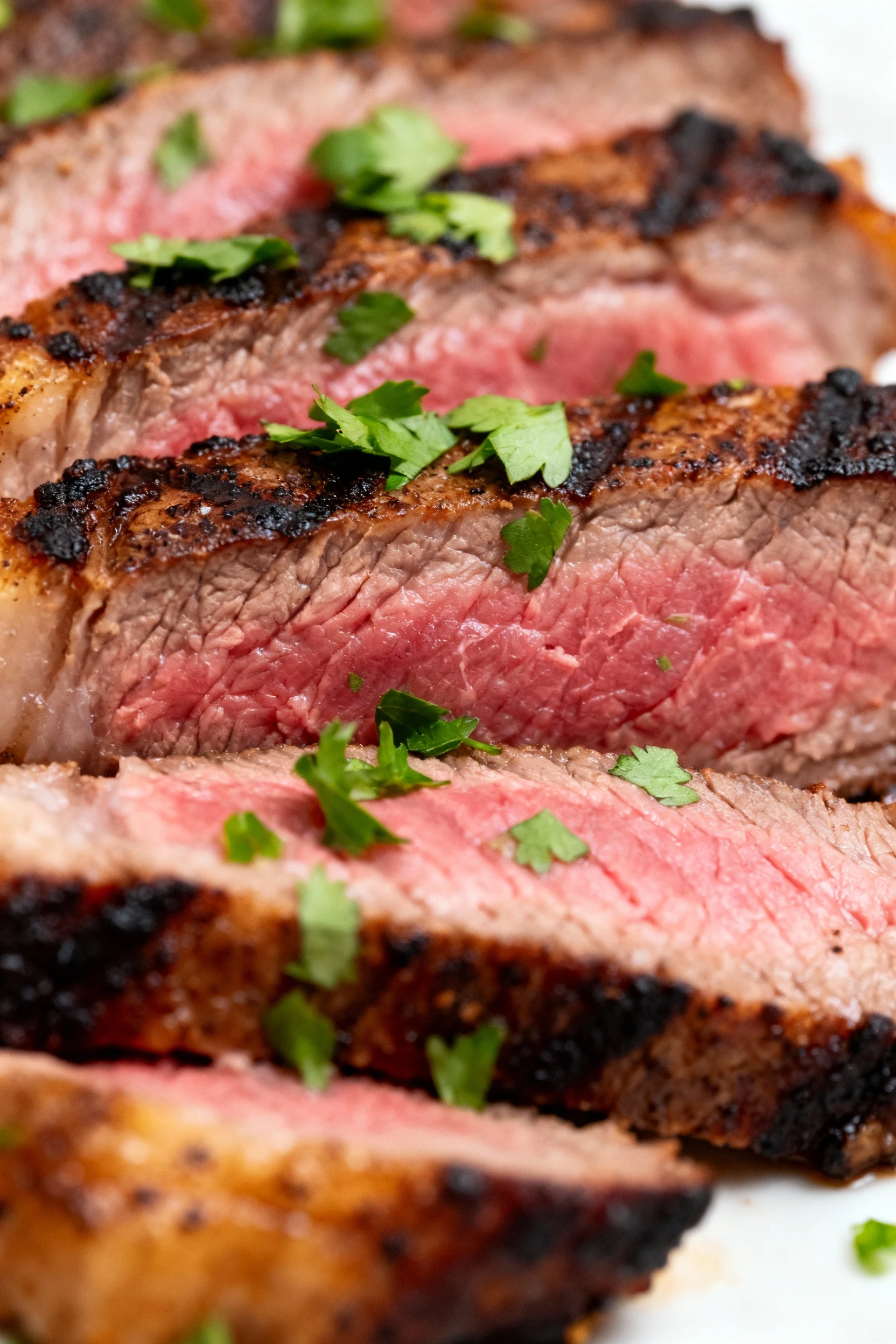 Close-up of perfectly seared London broil slices with visible charred edges and juicy pink center, garnished lightly wit