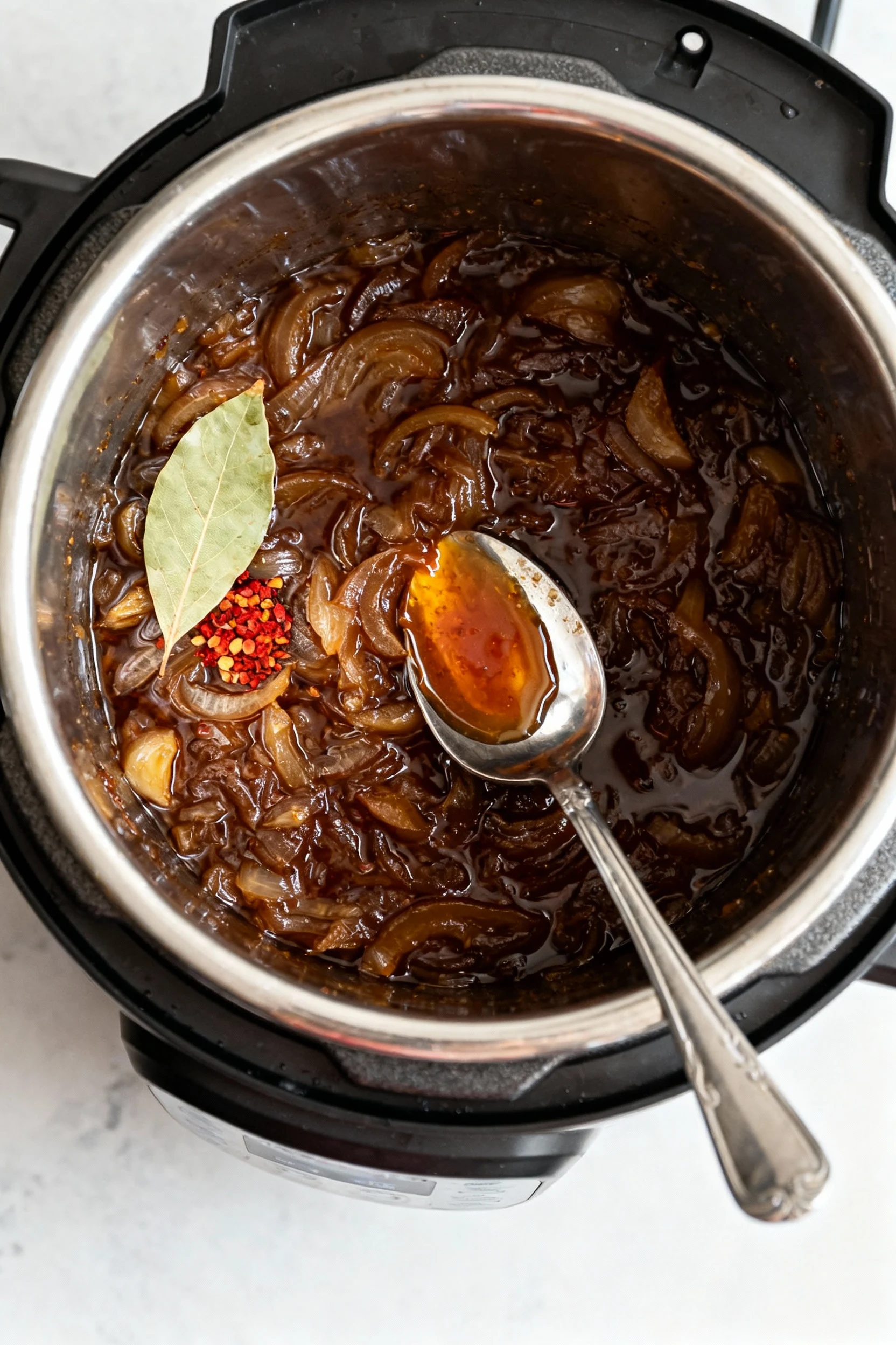 Food photography, Overhead cooking process in an Instant Pot on Sauté: dark amber onion jam simmering with a bay leaf an