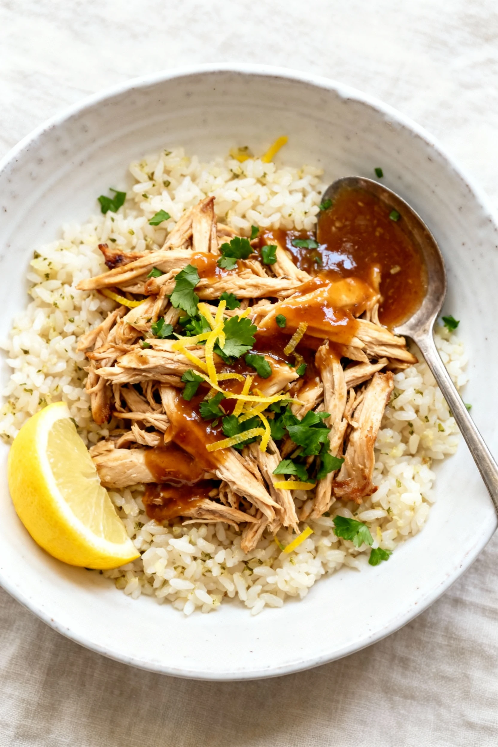 Overhead shot of juicy shredded chicken over garlic rice, spooned with glossy sauce, garnished with chopped parsley and 