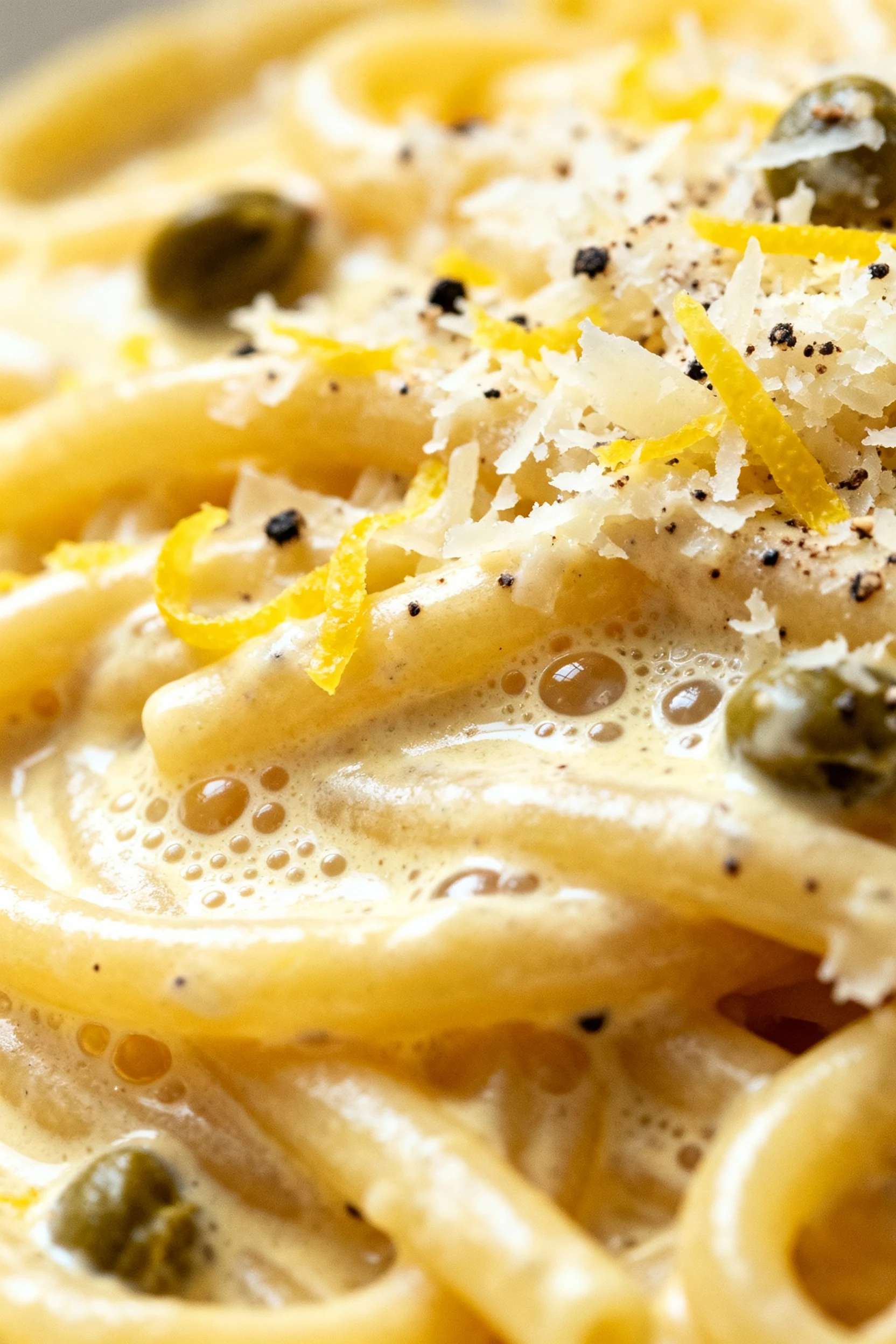 Extreme close-up of bucatini coated in silky lemon cream sauce with a butter sheen and micro-bubbles, finely grated Parm
