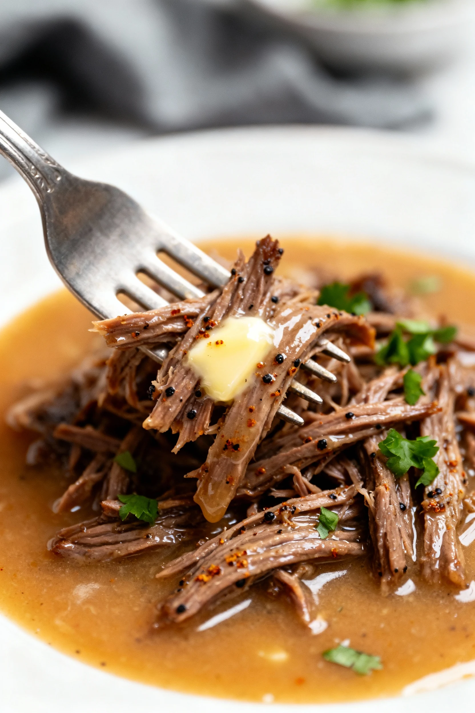 Close-up of fork-shredded chuck roast bathed in silky cornstarch-thickened gravy, glistening strands with black pepper a