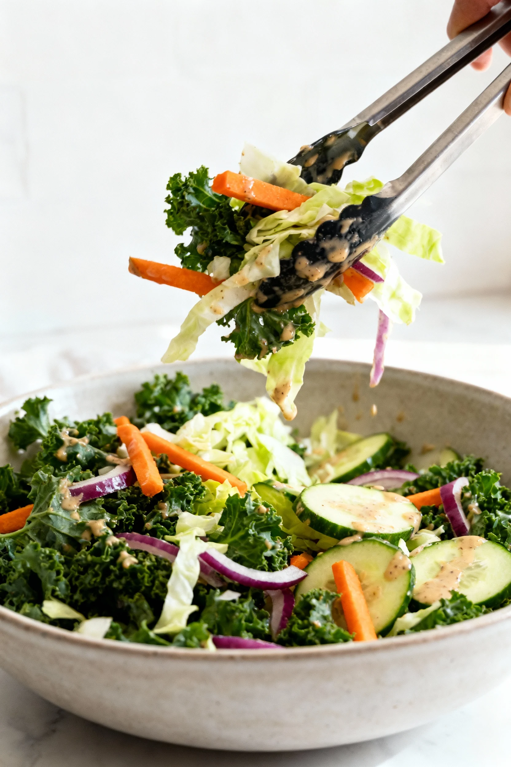 Three-quarter process shot of the base being tossed: kale, cabbage, carrot, cucumber, and red onion lightly coated with 