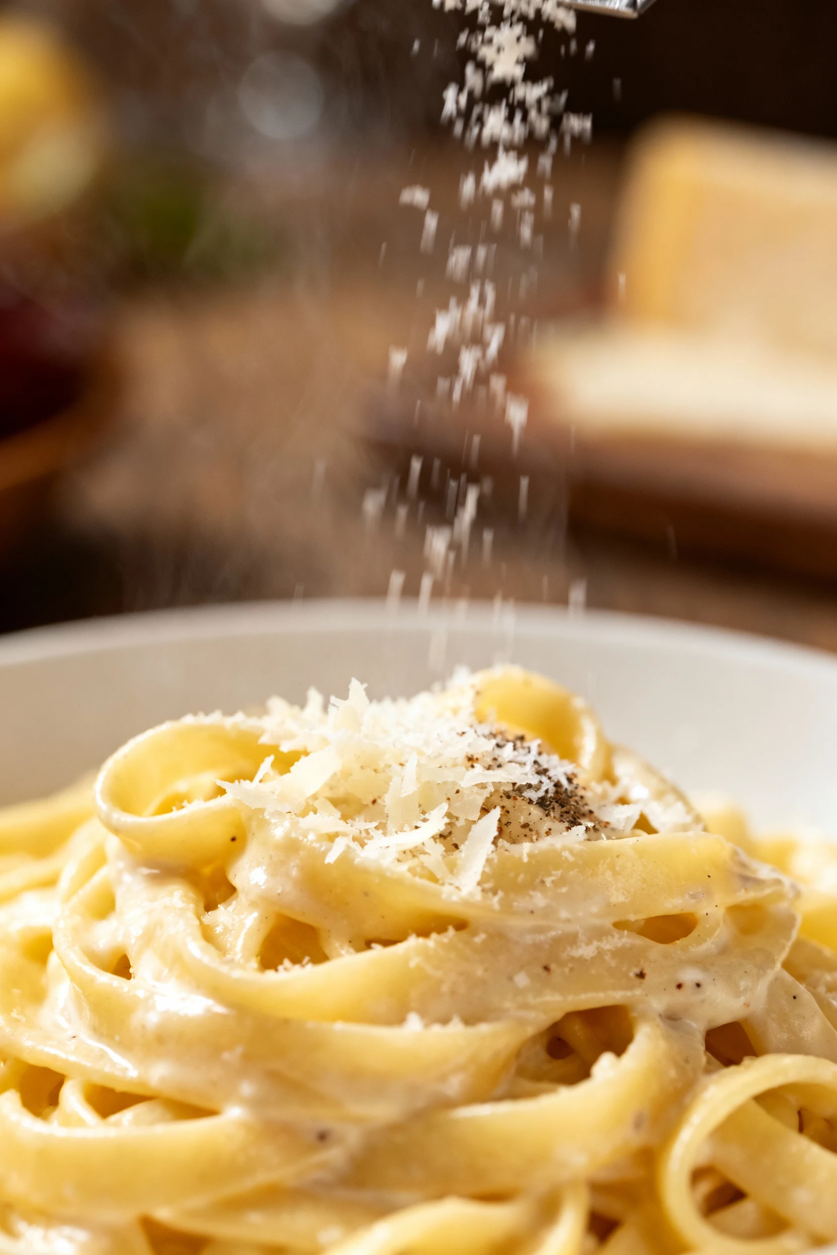 Close-up: fettuccine Alfredo being tossed with hot pasta water—silky, creamy coating, microplaned Parmesan melting, hint