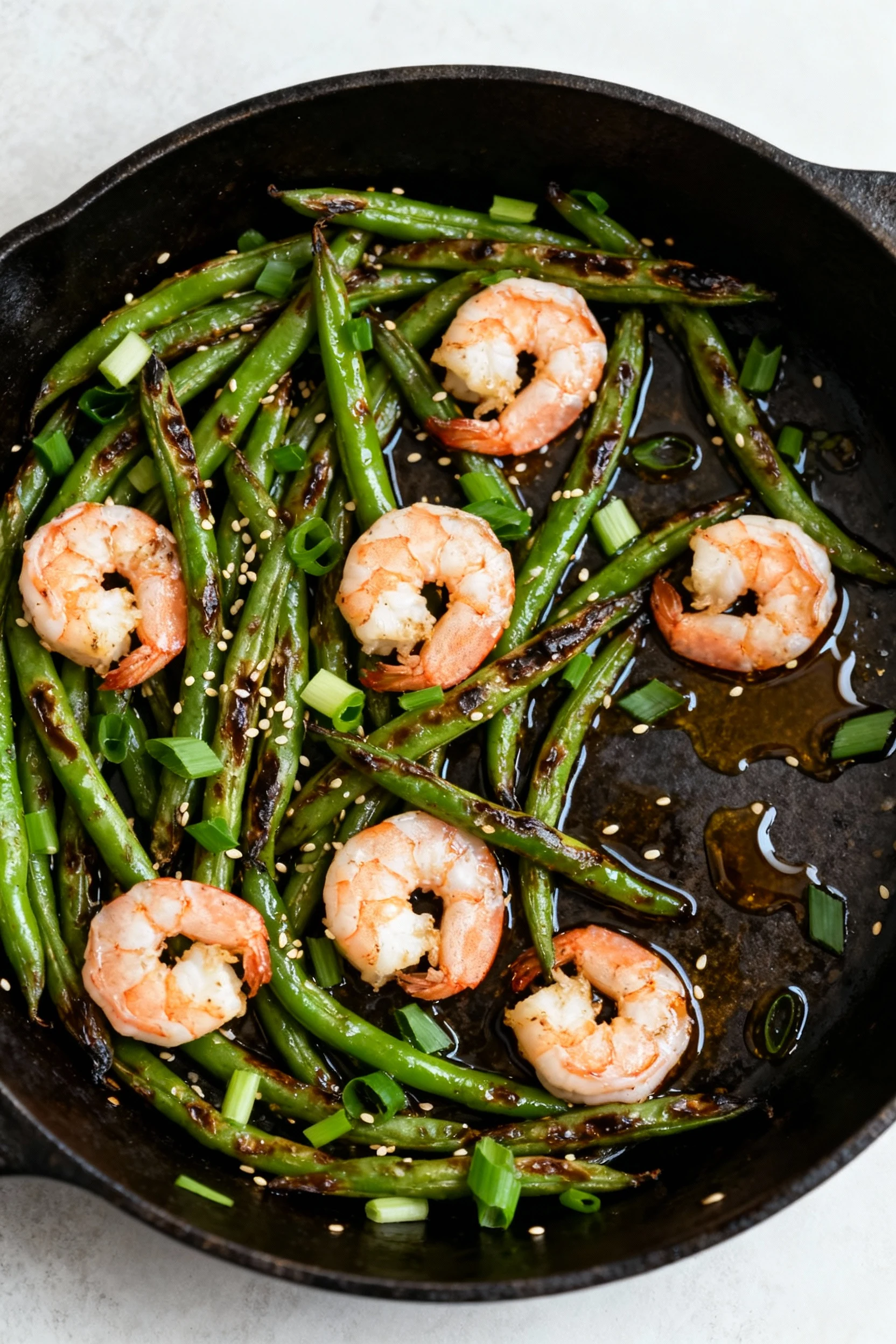 Tasty top view: Shrimp & Garlic Green Beans, overhead in a dark skillet; blistered green beans and pink shrimp with sesa