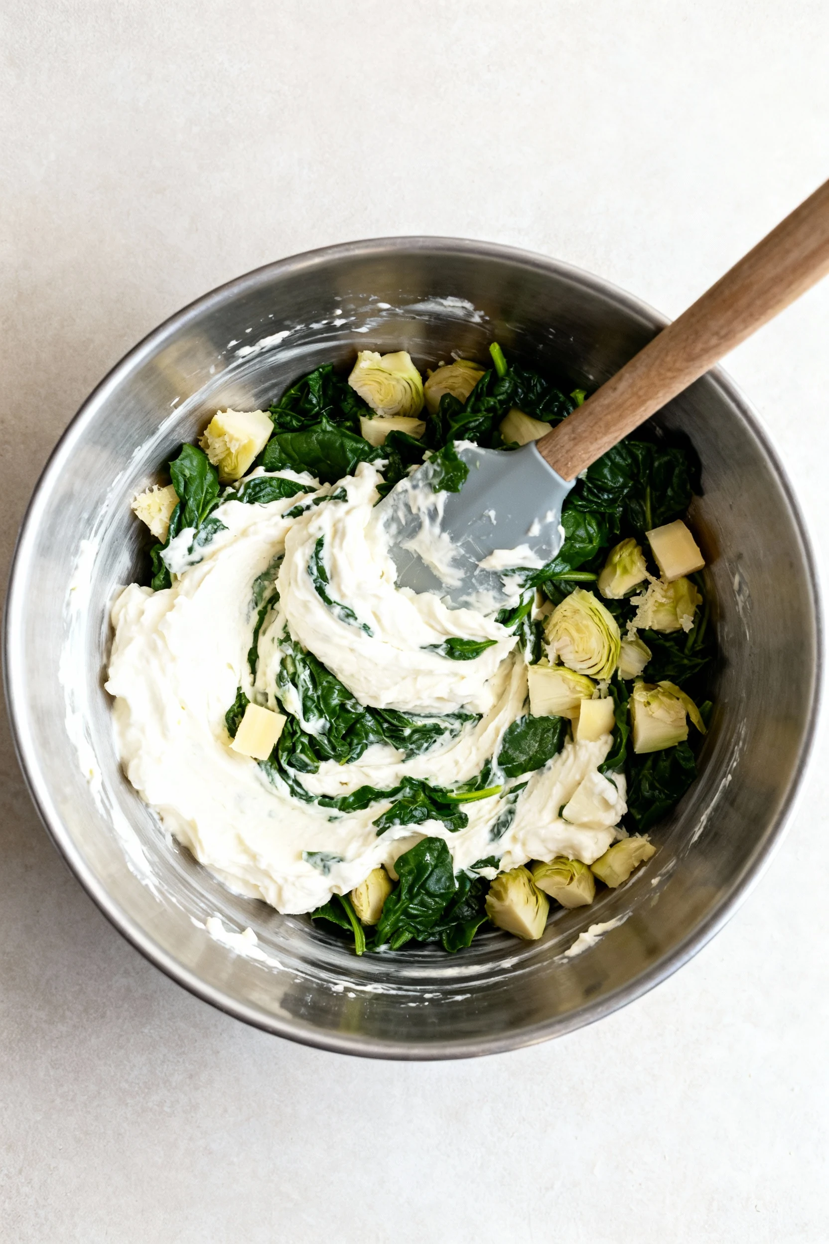 Cooking process overhead: silky cream cheese base (with sour cream, mayo, mozzarella, Parmesan) being folded with bone-d
