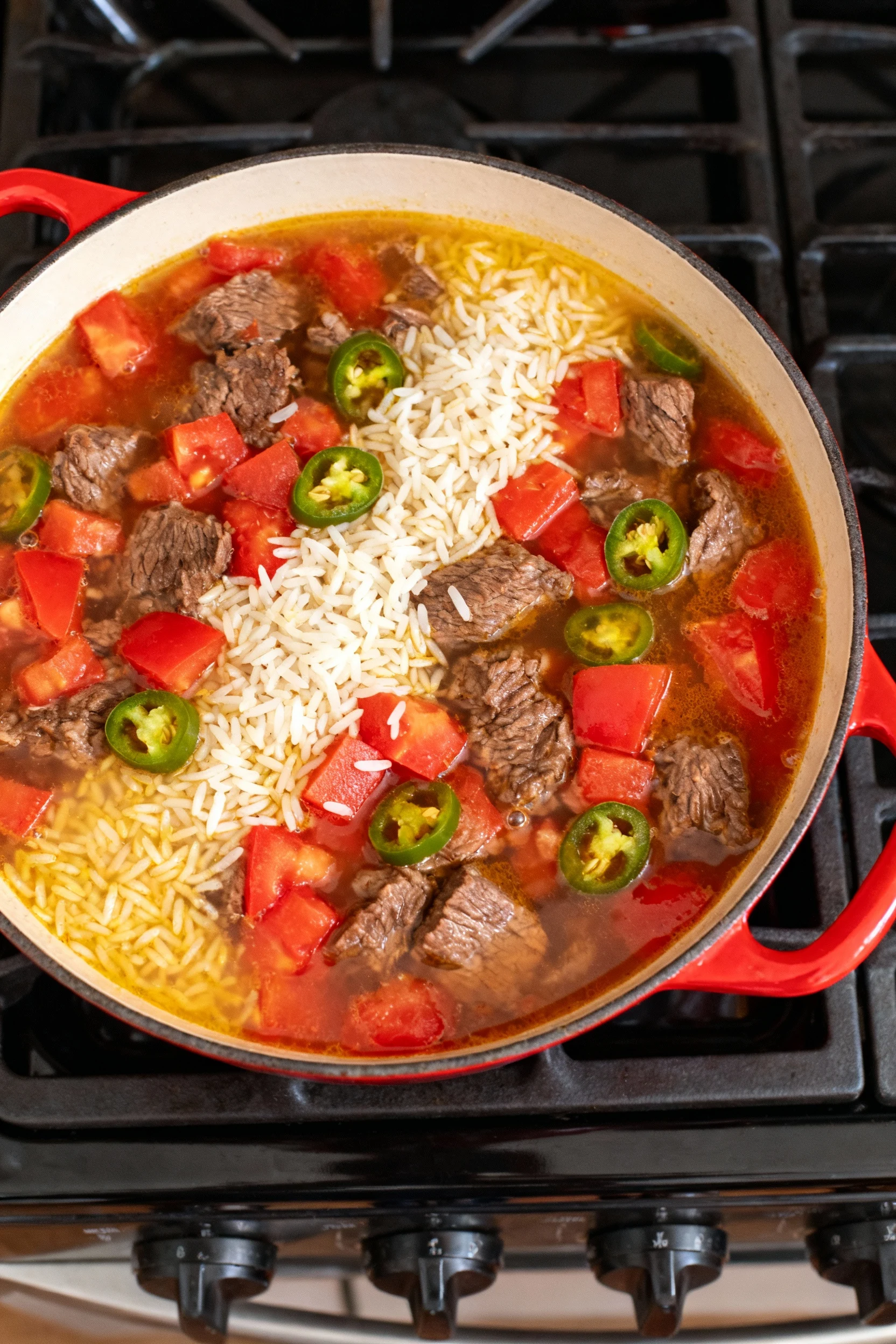 Overhead simmer shot: beef, rice, and diced tomatoes with green chilies bubbling in broth; vibrant reds and yellows, flu