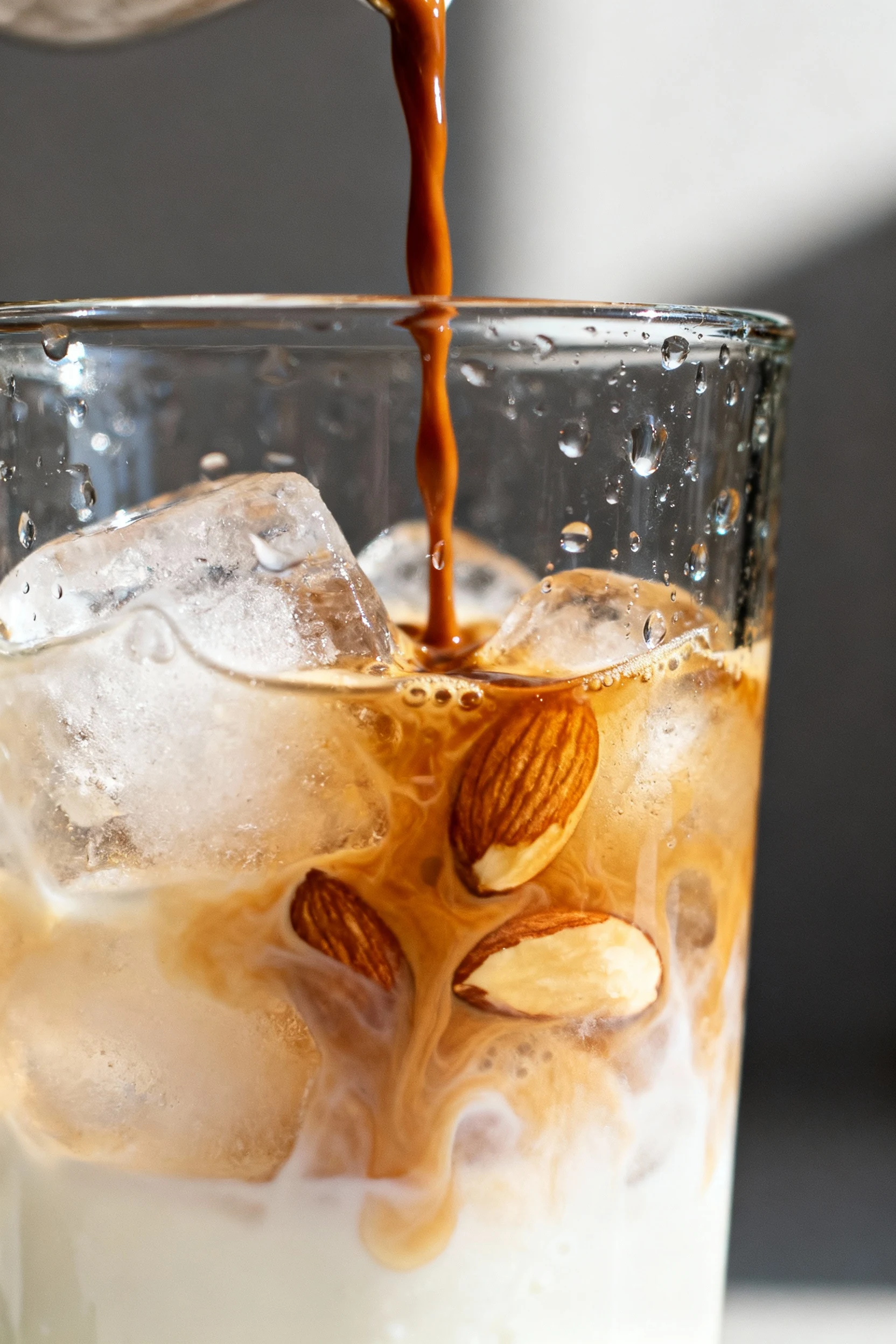 3. Dramatic macro shot of espresso cascading into a chilled glass partially filled with ice, rich caramel tones blending