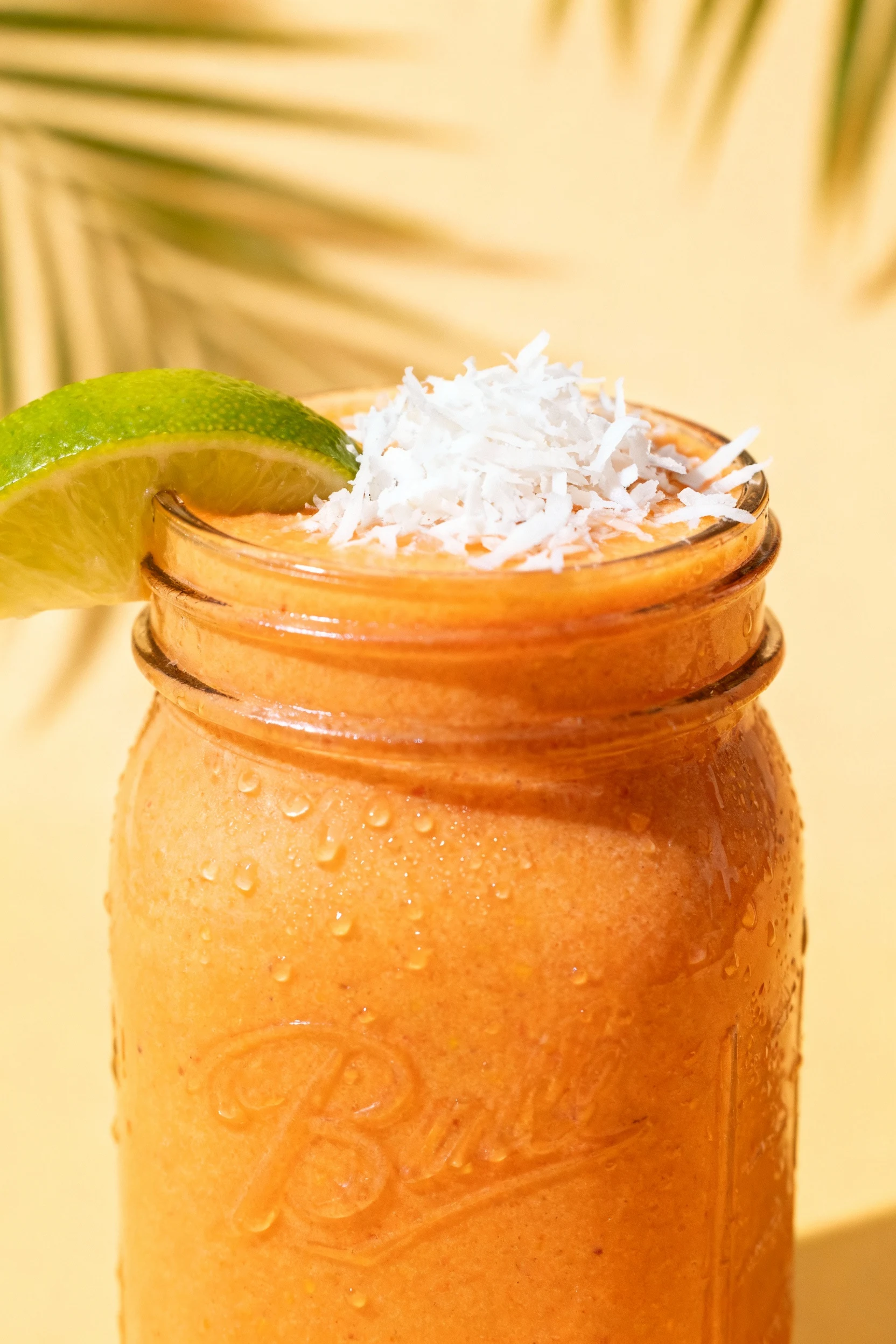 Beautifully plated Tropical Gut-Soother smoothie in a chilled glass jar, sunny orange-yellow tone with shredded coconut 