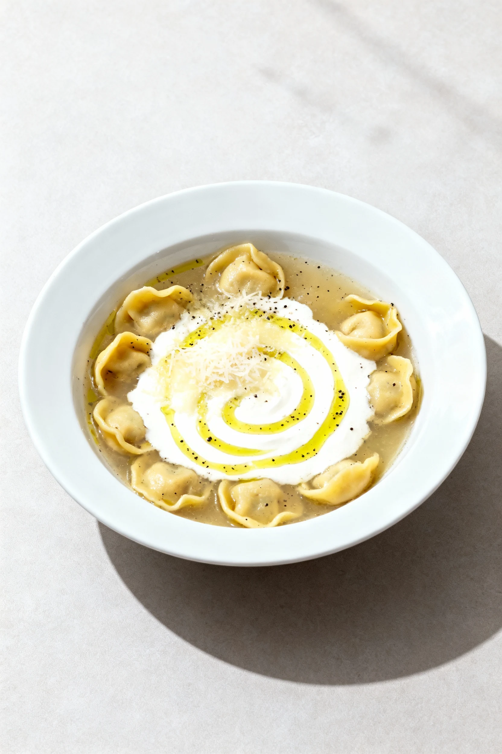 Food photography, Final plated presentation: tortellini soup with visible cream swirl and melted Parmesan in a modern wh