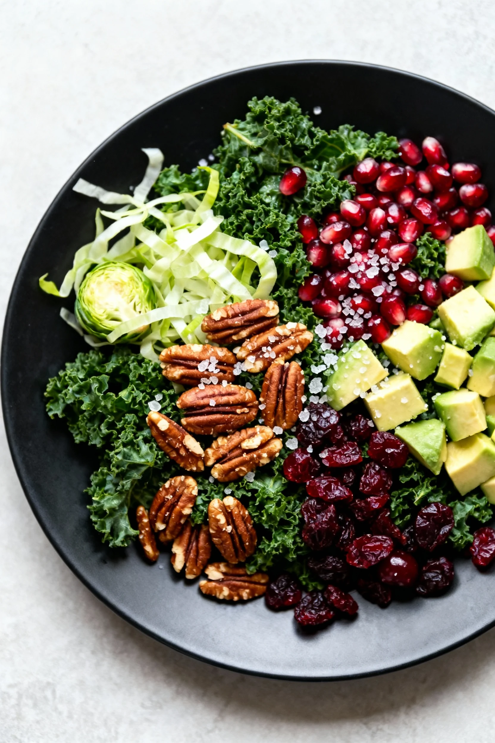Final presentation: vegan holiday kale salad plated on a matte black platter - massaged kale, shaved Brussels, candied p