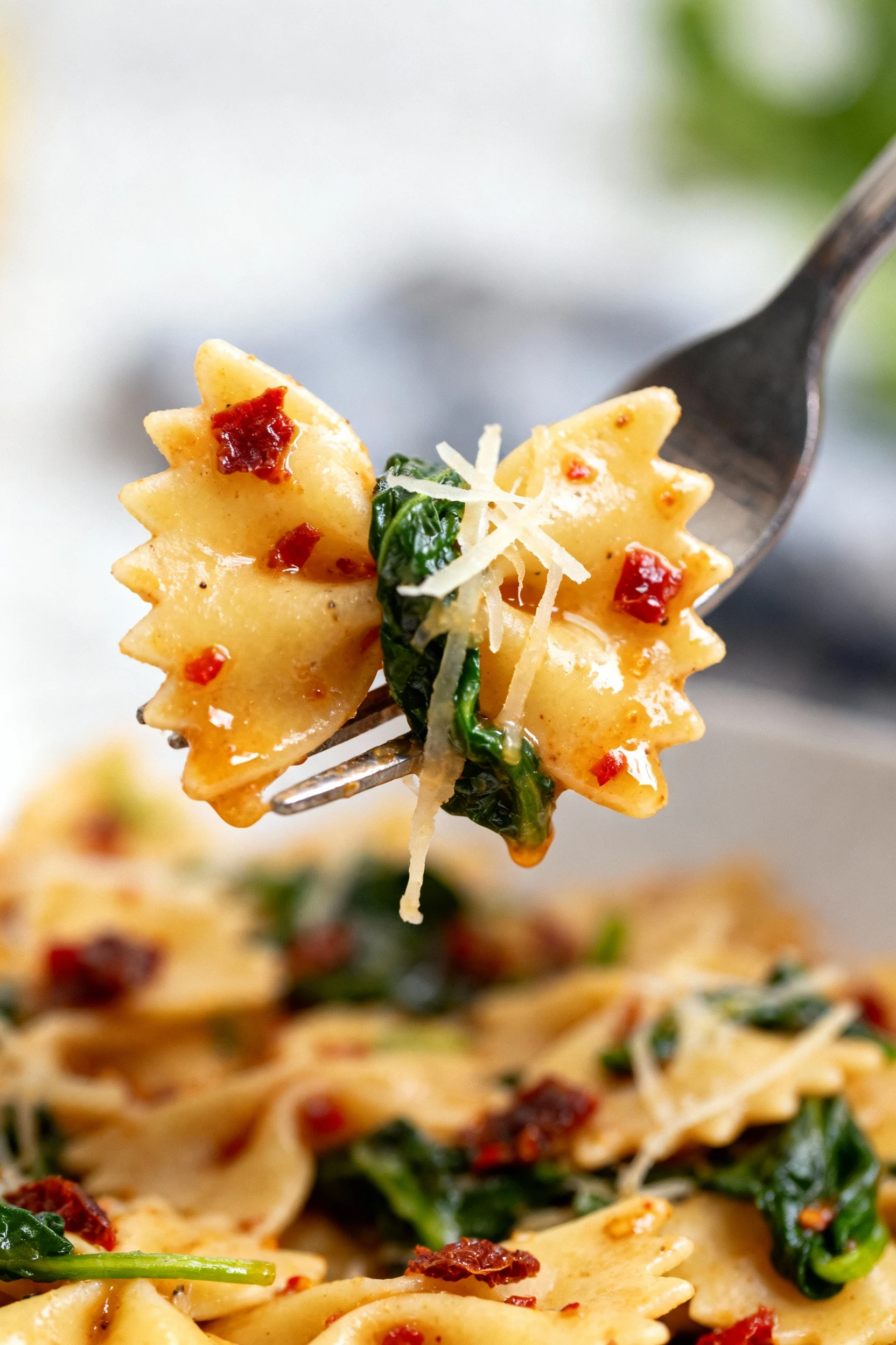 Extreme close-up detail: bowtie pasta on a fork with sauce clinging in the “wings,” flecks of sun-dried tomato and red p