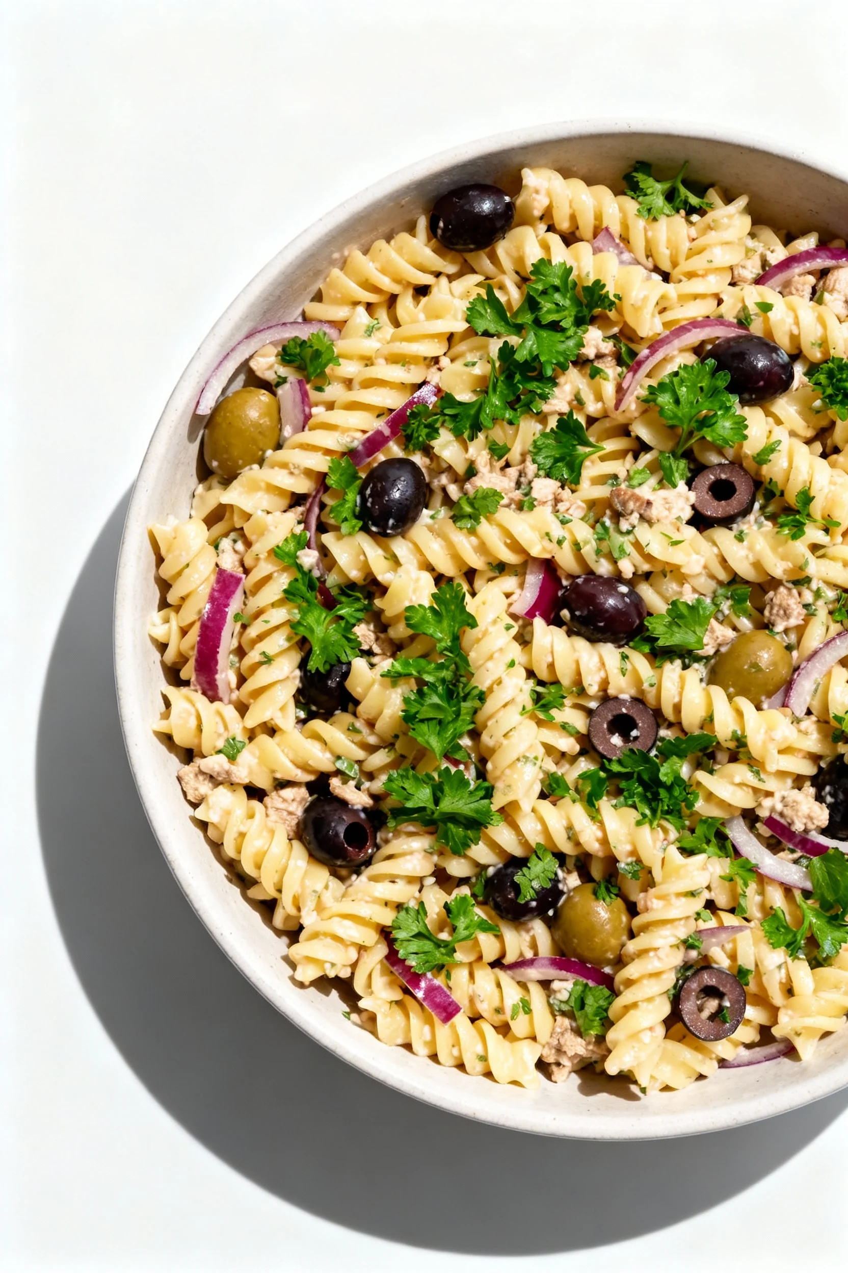 Overhead shot of a large serving bowl filled with fully assembled pasta salad, parsley sprinkled on top, olives and red 