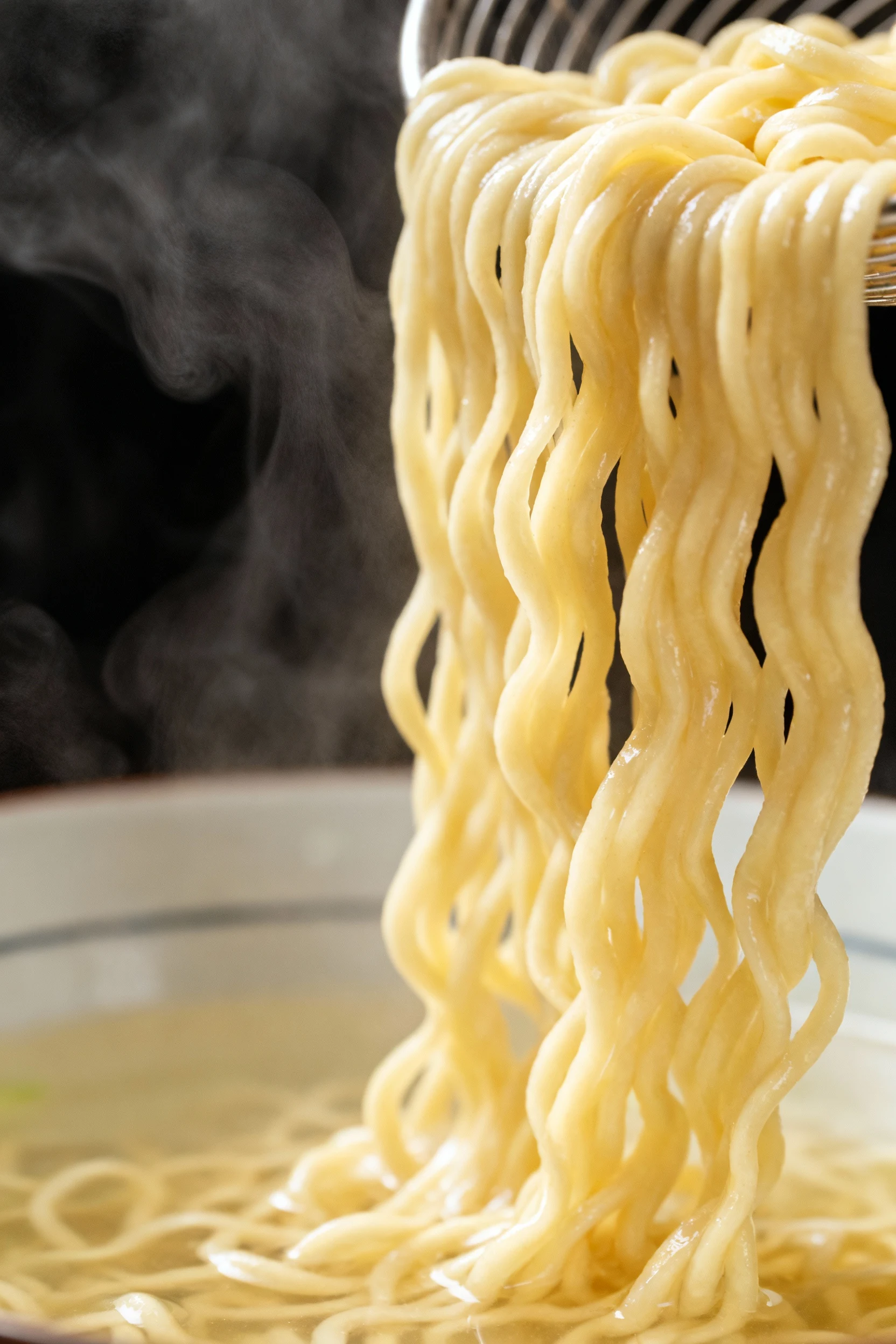 Close-up process: freshly cooked ramen noodles drained separately and glistening, slightly underdone for bounce; steam v