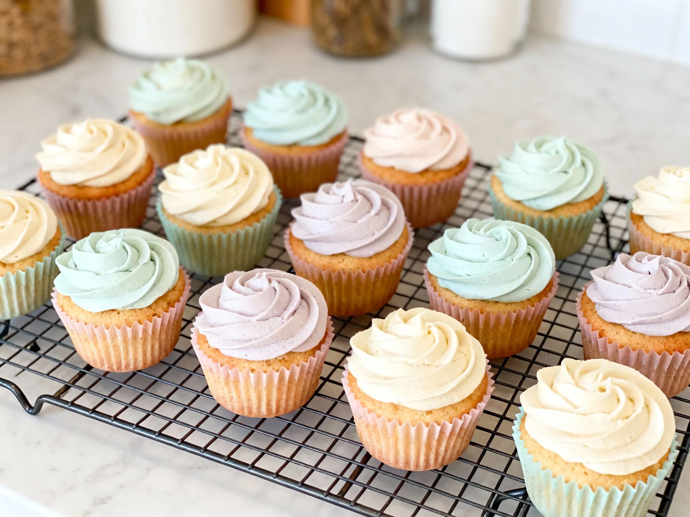 Food photography, Overhead shot of a dozen cooled cupcakes in pastel paper liners arranged neatly on a wire rack, each t