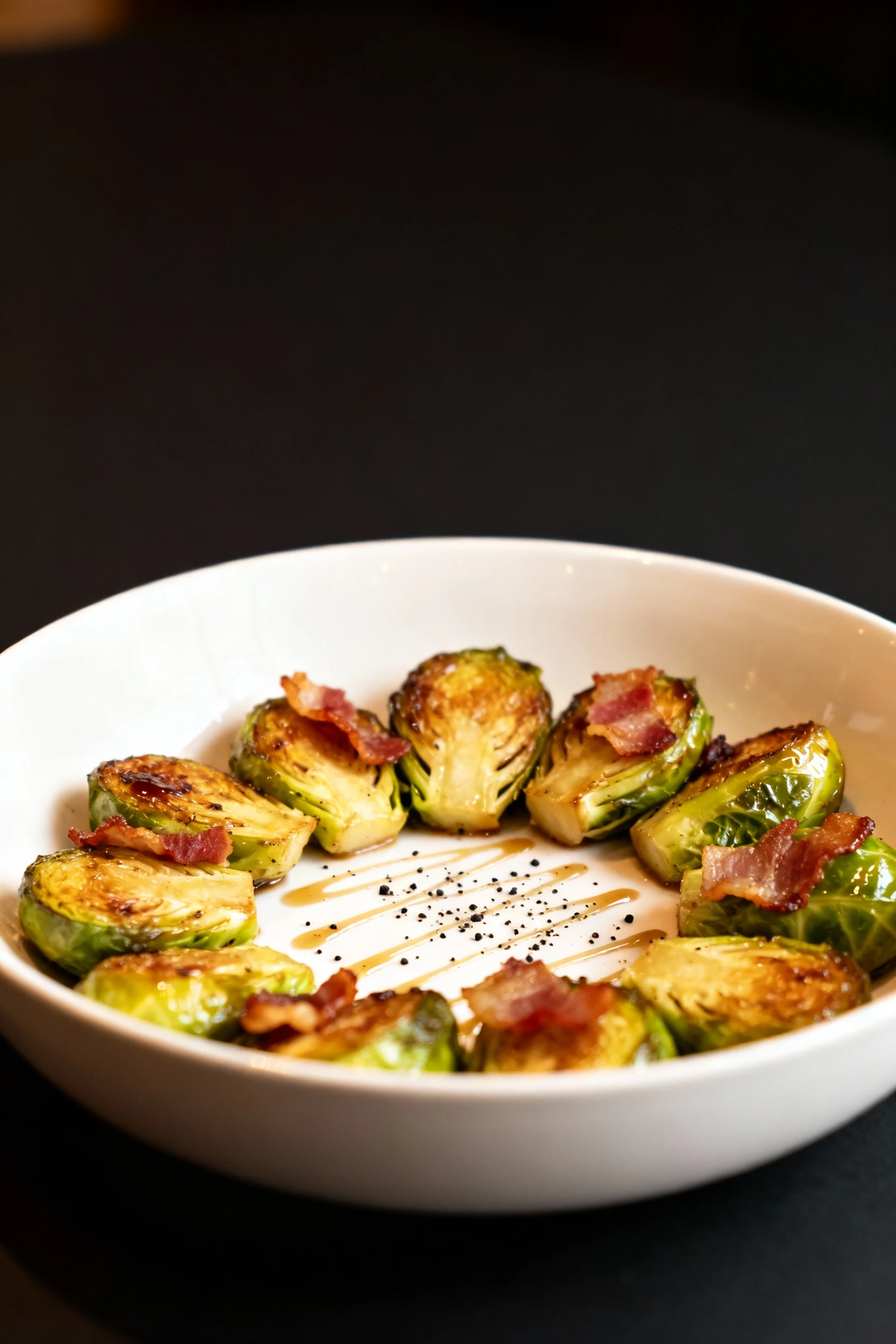 Restaurant-style final presentation of brussel sprouts and bacon served in a shallow white bowl, garnished with fresh cr