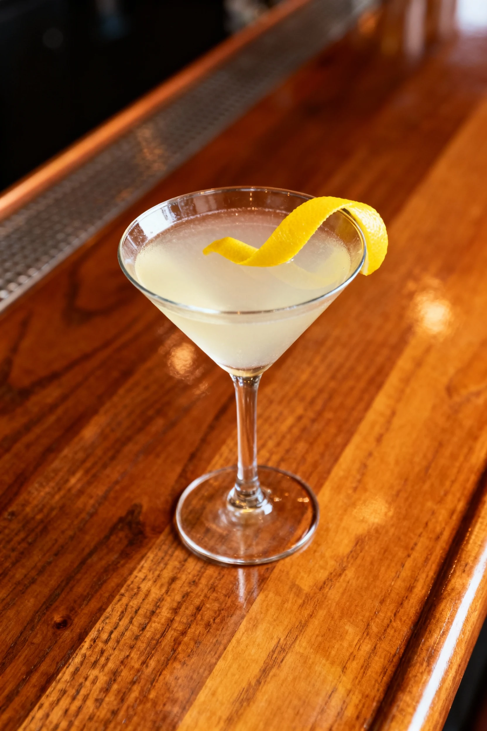 Top-down view of a vibrant lemon-twist martini, bright yellow ribbon of citrus floating atop the pale drink, glass set o