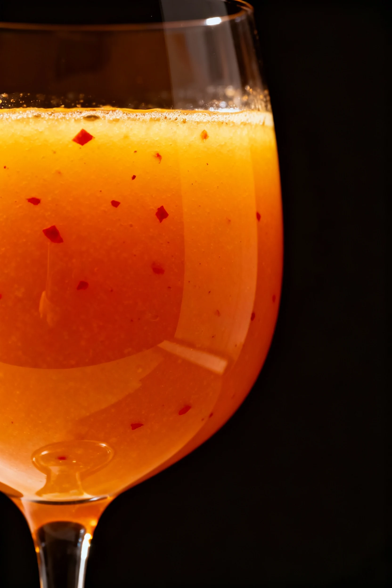 6. Close-up side view of spicy kick variation—cayenne-spiced carrot-pineapple juice in a sleek glass, tiny red specks vi