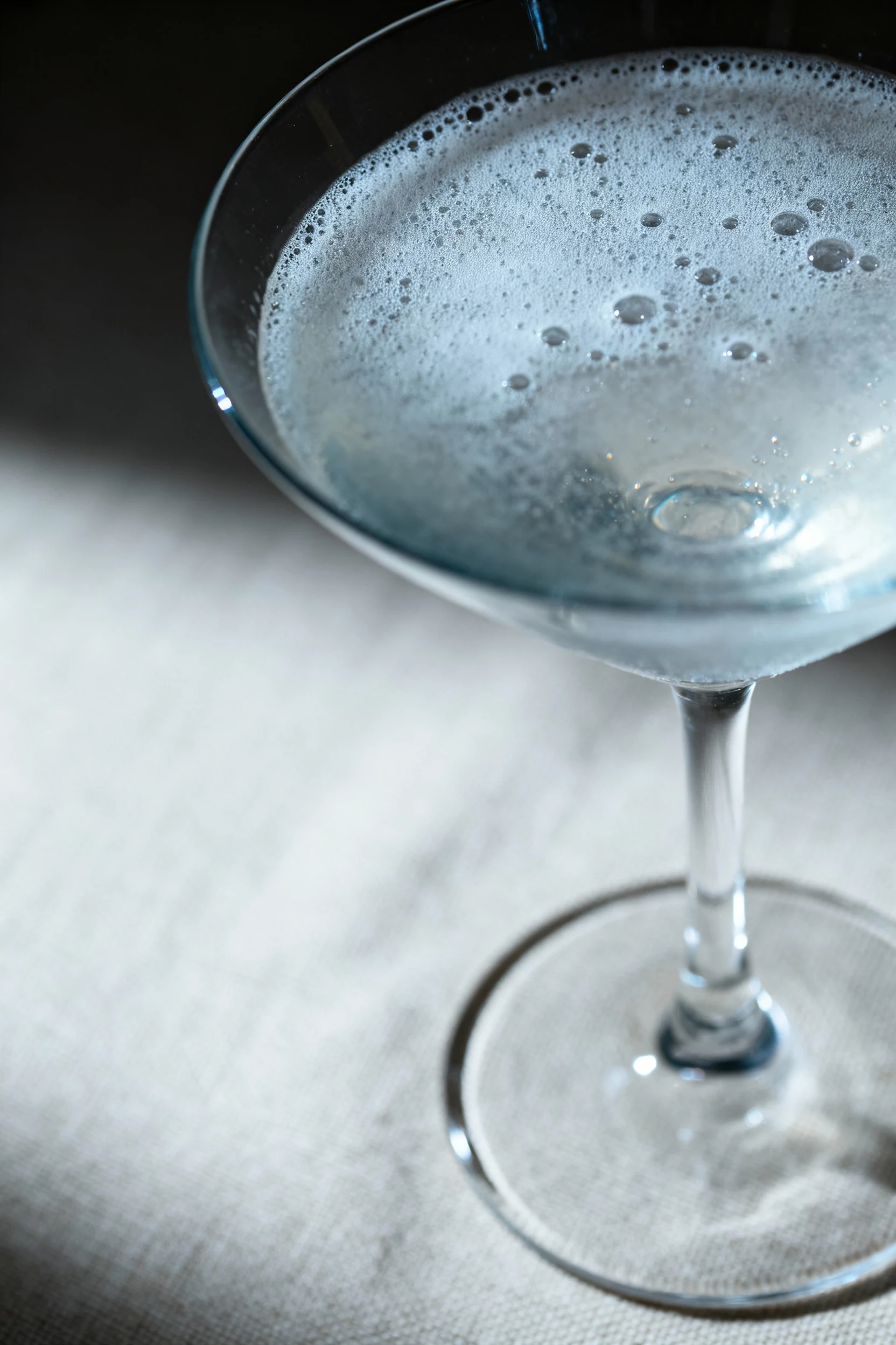 Macro shot showcasing the frothy, slightly clouded surface of a shaken vesper martini, tiny air bubbles catching ambient