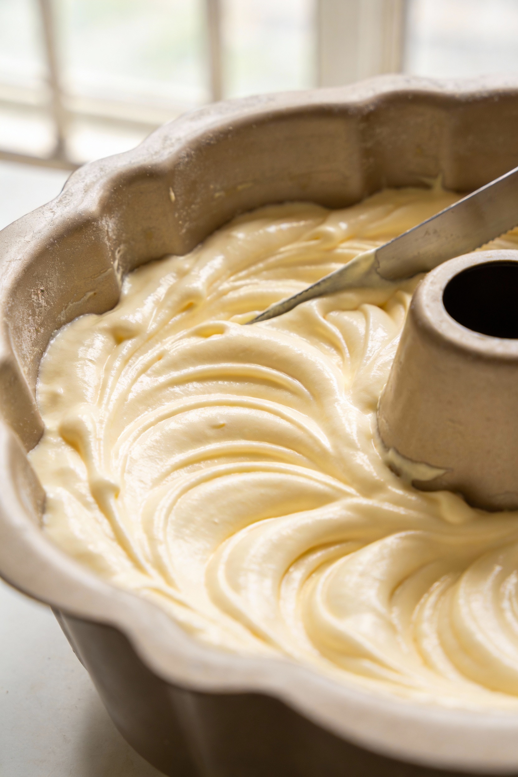 Close-up detail of glossy stiff-peaked angel food cake batter smoothed in an ungreased tube pan, subtle spatula swirls a