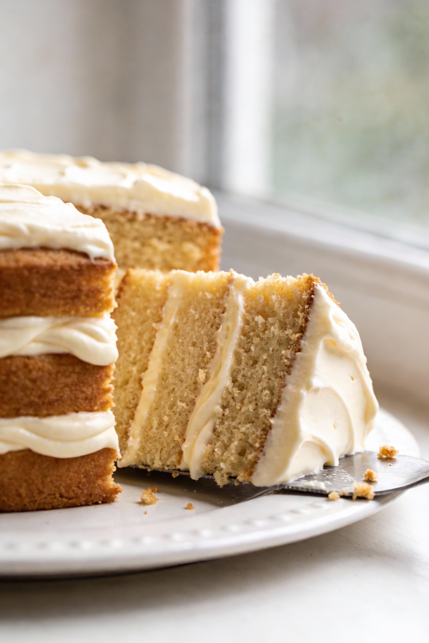 Close-up detail of a sliced gluten-free vanilla layer cake showing a plush, tender crumb (no grit), thick vanilla butter
