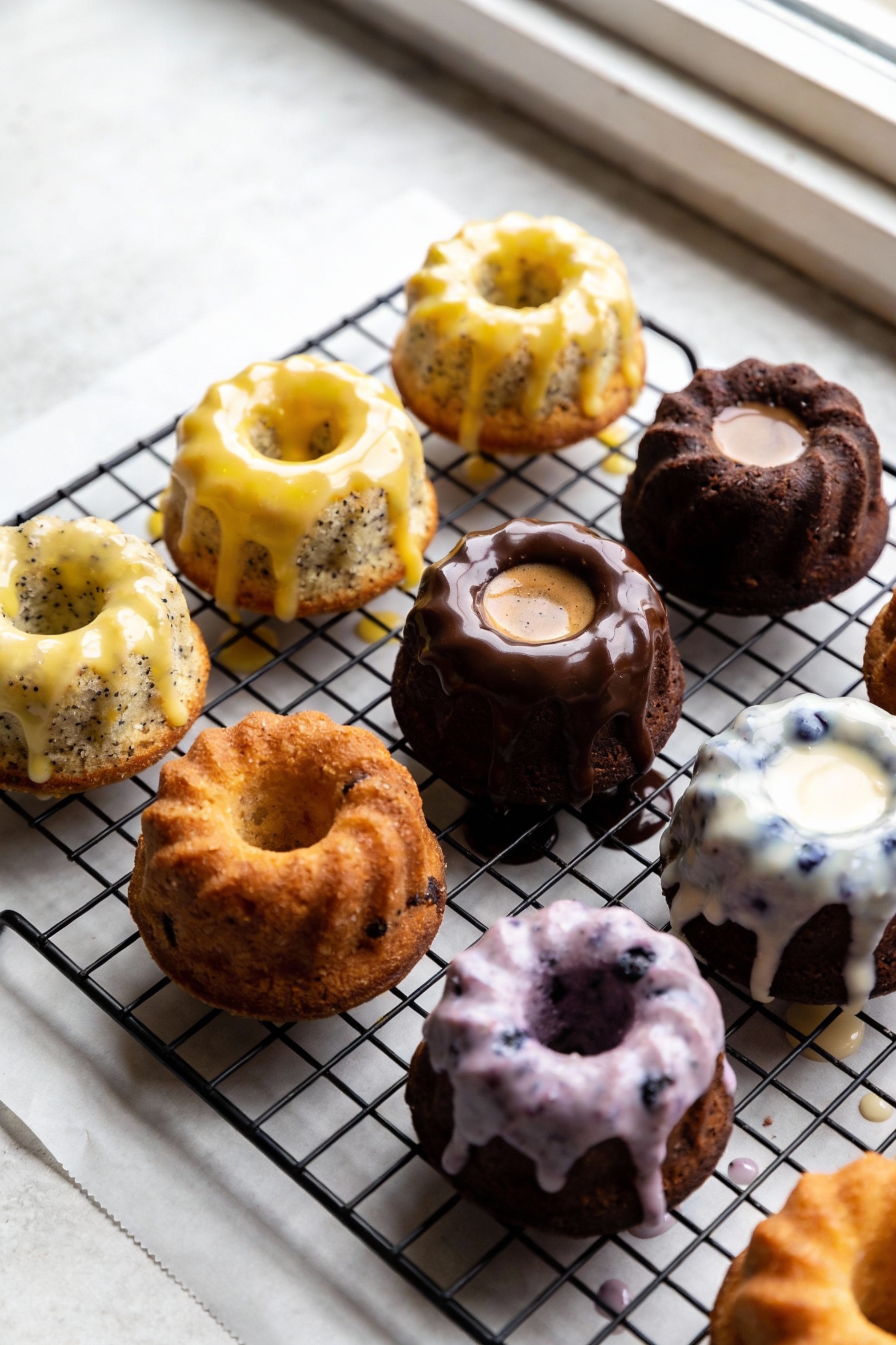 Overhead shot of a cooling rack filled with assorted mini Bundt cakes (lemon poppy seed, chocolate espresso, blueberry y