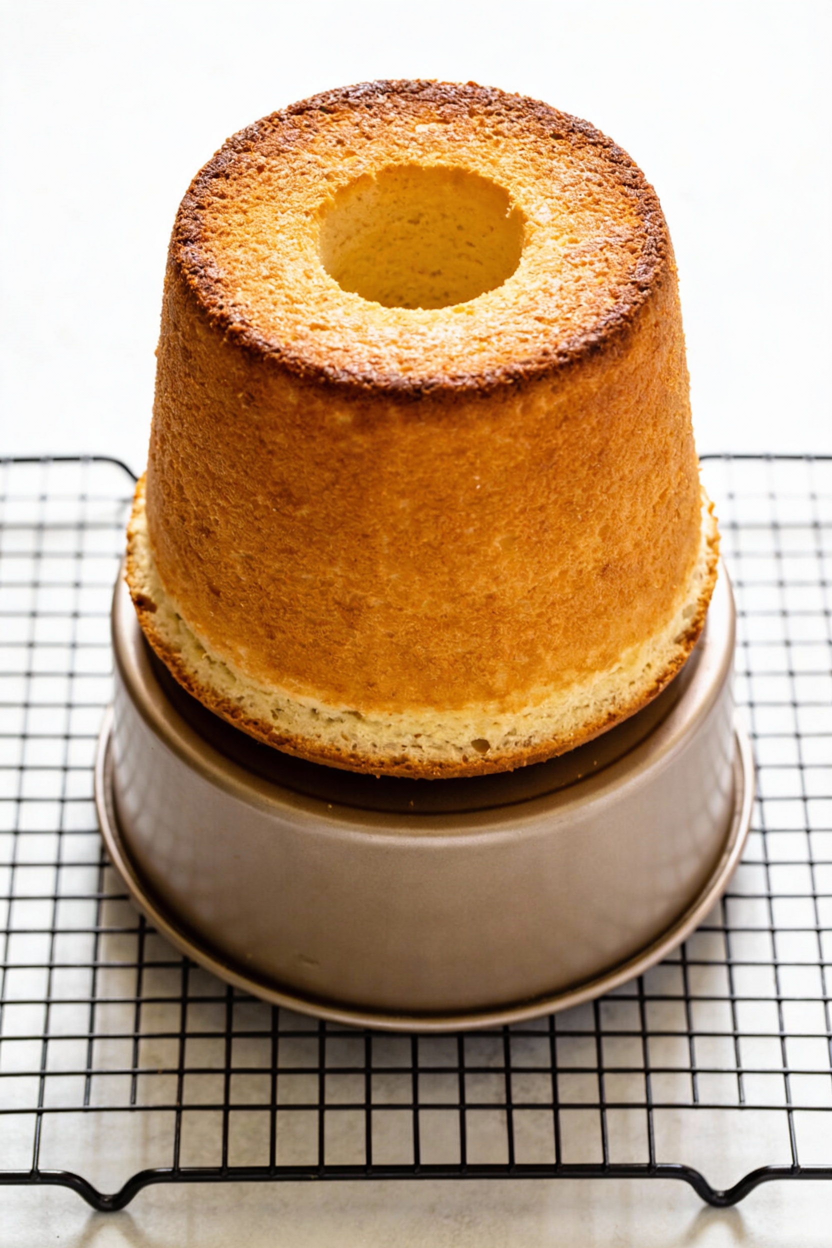 Overhead shot of a golden-baked angel food cake cooling upside down in its tube pan set on its feet, tall domed top and