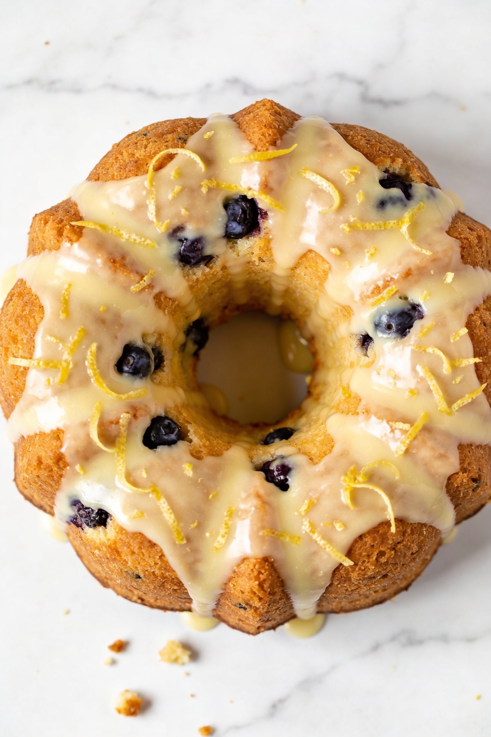 Tasty top view: Overhead shot of Lemon Blueberry Bundt—thin glossy lemon icing dripping over the ridges, lemon zest spri