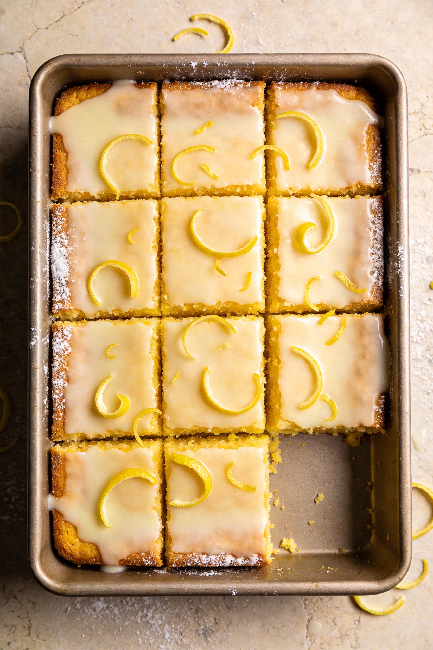 Overhead shot of neatly cut lemon cake squares in a 9x13 pan, glaze set to a smooth sheen, bright yellow crumb visible o