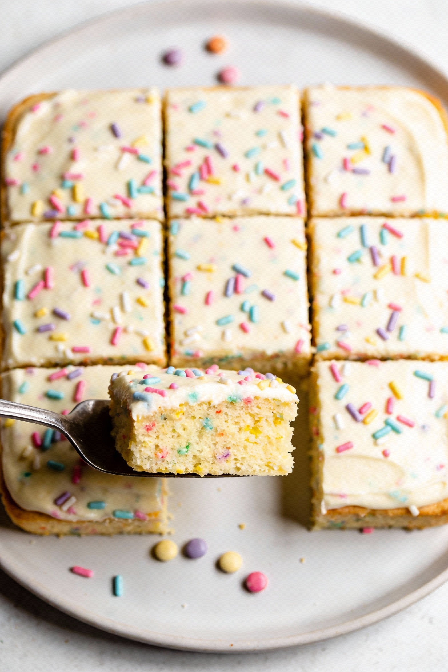 2. Overhead shot of a vegan vanilla funfetti sheet cake cut into neat squares, pastel vegan sprinkles scattered on top w