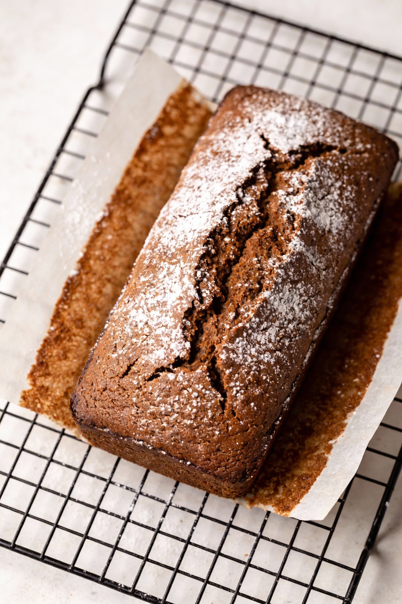 Overhead shot of the cozy gingerbread loaf cake cooling on a wire rack, lightly dusted with powdered sugar, warm brown c