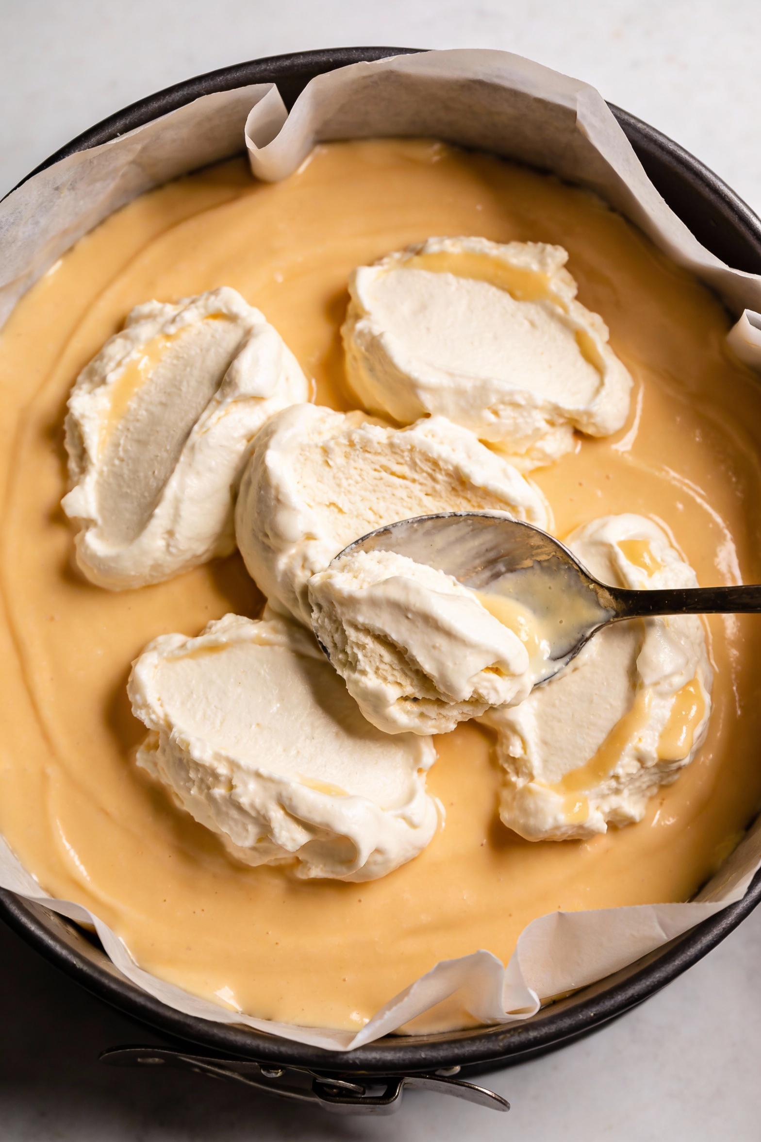 Overhead shot of the cake assembly in a parchment-lined 9-inch springform pan: smooth warm (not hot) custard layer sprea