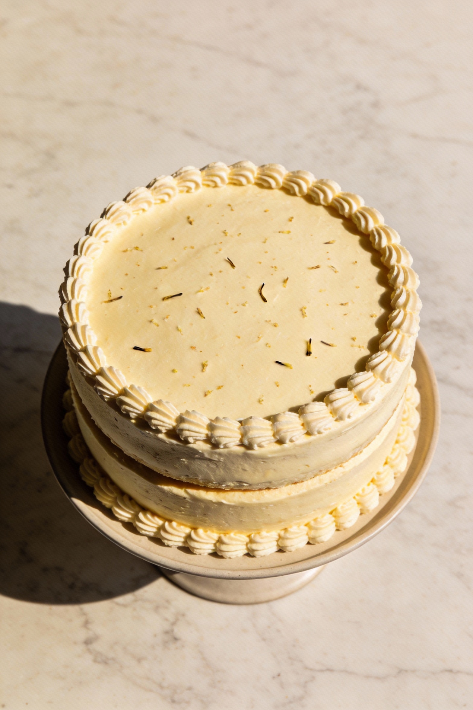 Overhead shot of a fully assembled two-layer vanilla cake on a simple cake stand, smooth buttercream finish with a neat 