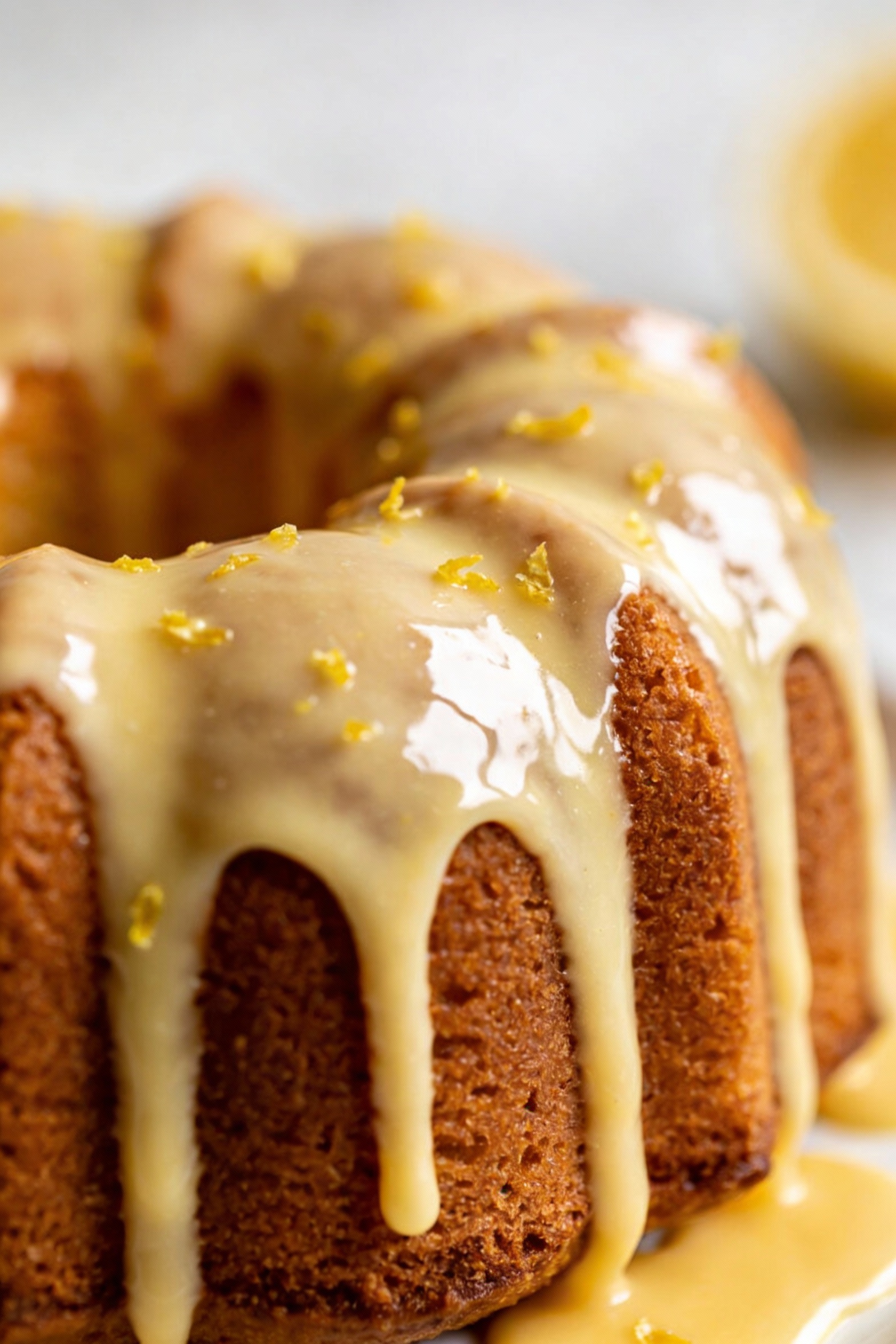 Close-up detail of thick vanilla-lemon glaze cascading over Bundt cake grooves, highlighting the shiny set surface and t