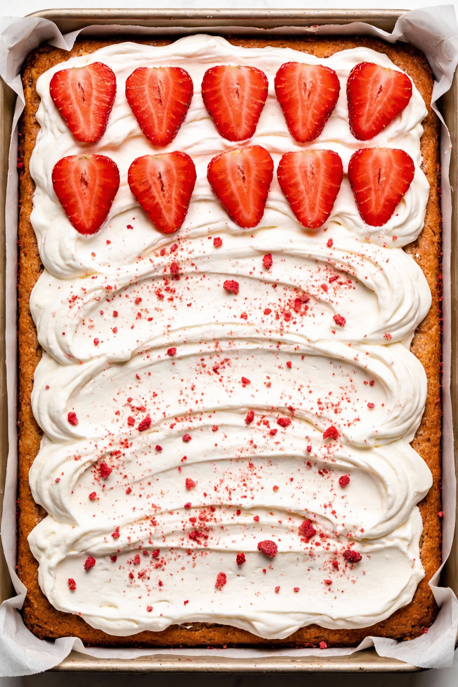 2. Overhead shot of a frosted 9x13 bakery-style strawberry sheet cake in the pan, smooth cream cheese frosting swirls, s