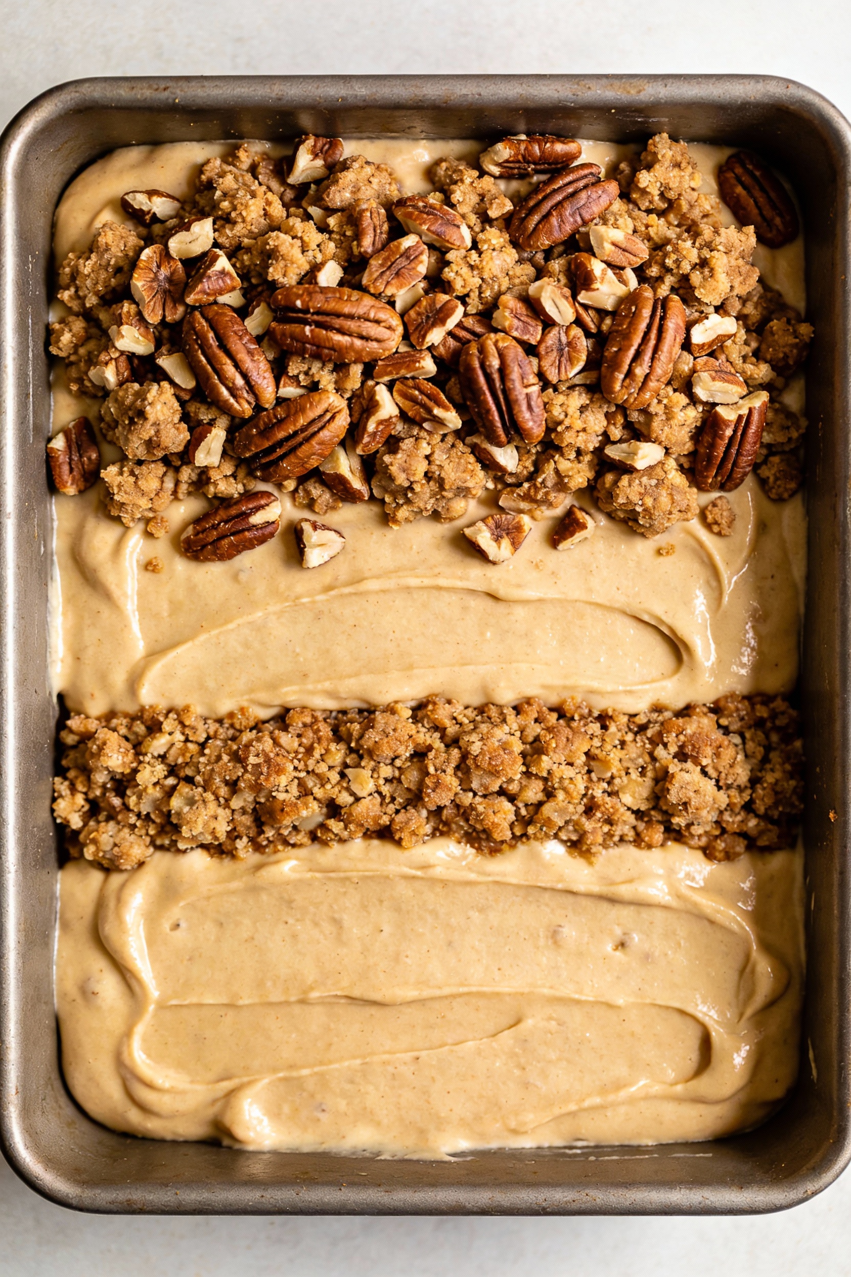 3. Cooking process photo of the fully assembled unbaked coffee cake in the pan: thick batter spread in layers with a vis