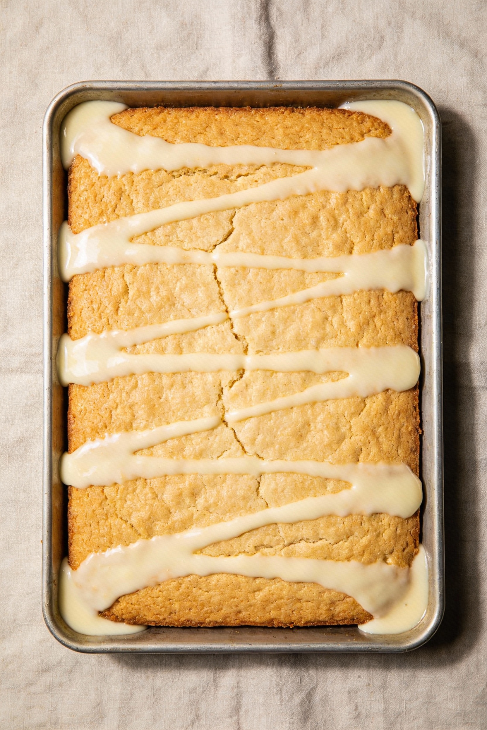 3. Tasty top view: 9x13 vanilla snack cake with glossy vanilla glaze drizzled in ribbons, glaze pooling slightly in corn