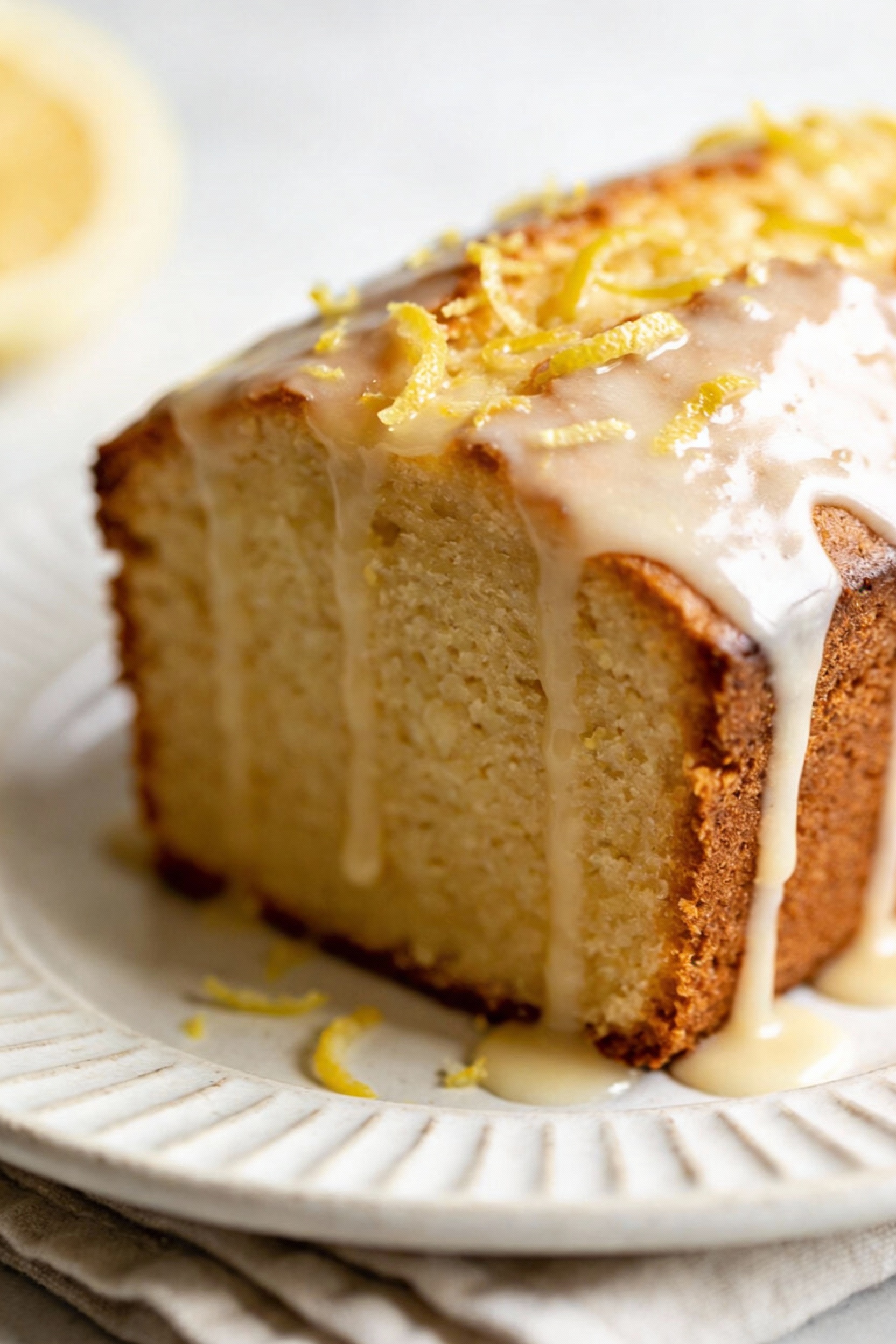 Beautifully plated lemon-glazed cake wedge on a white ceramic plate, thin translucent glaze dripping down the sides with