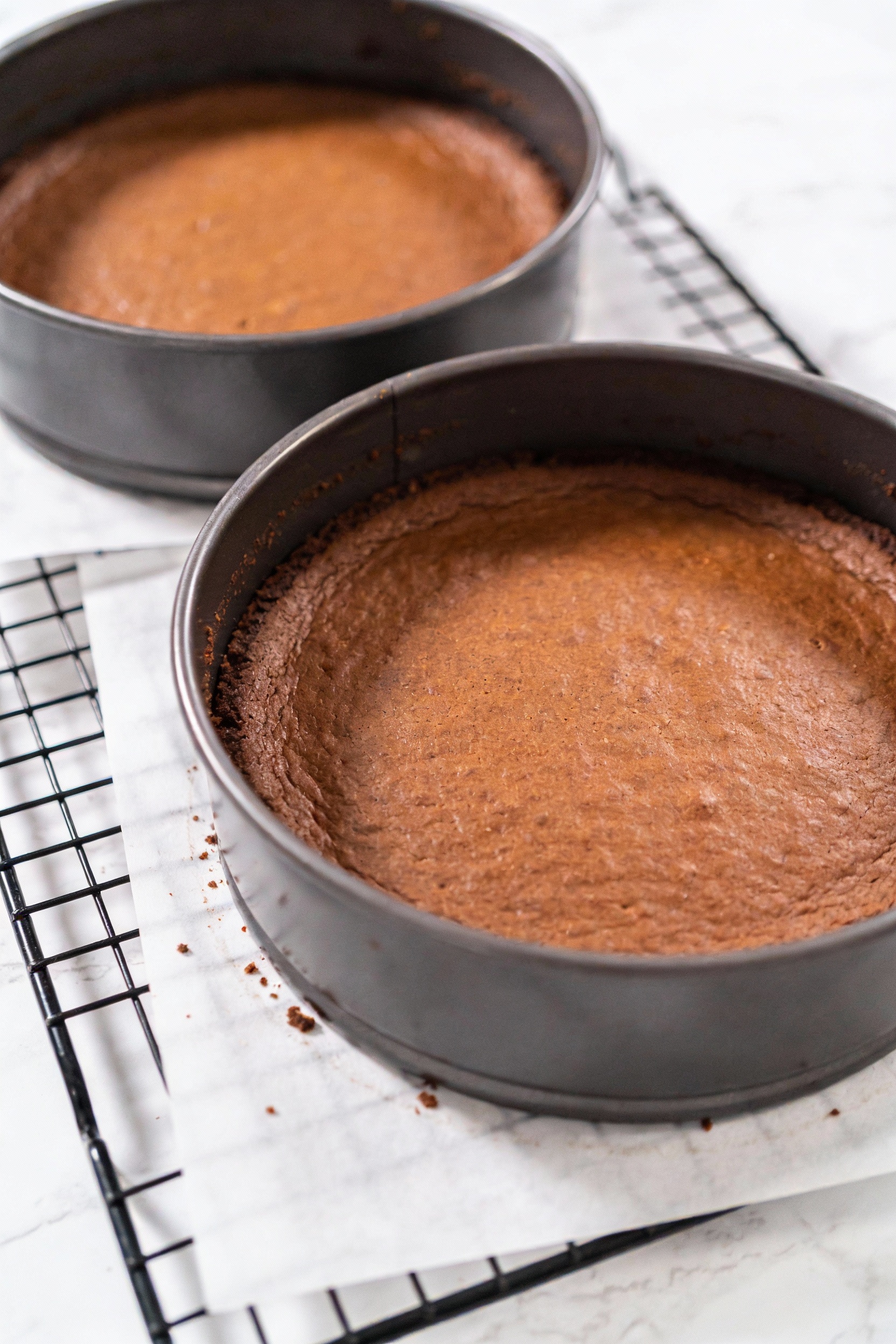 Cooking process: Two chocolate 8-inch cake layers just baked, cooling on parchment-lined racks—level tops, edges pulling