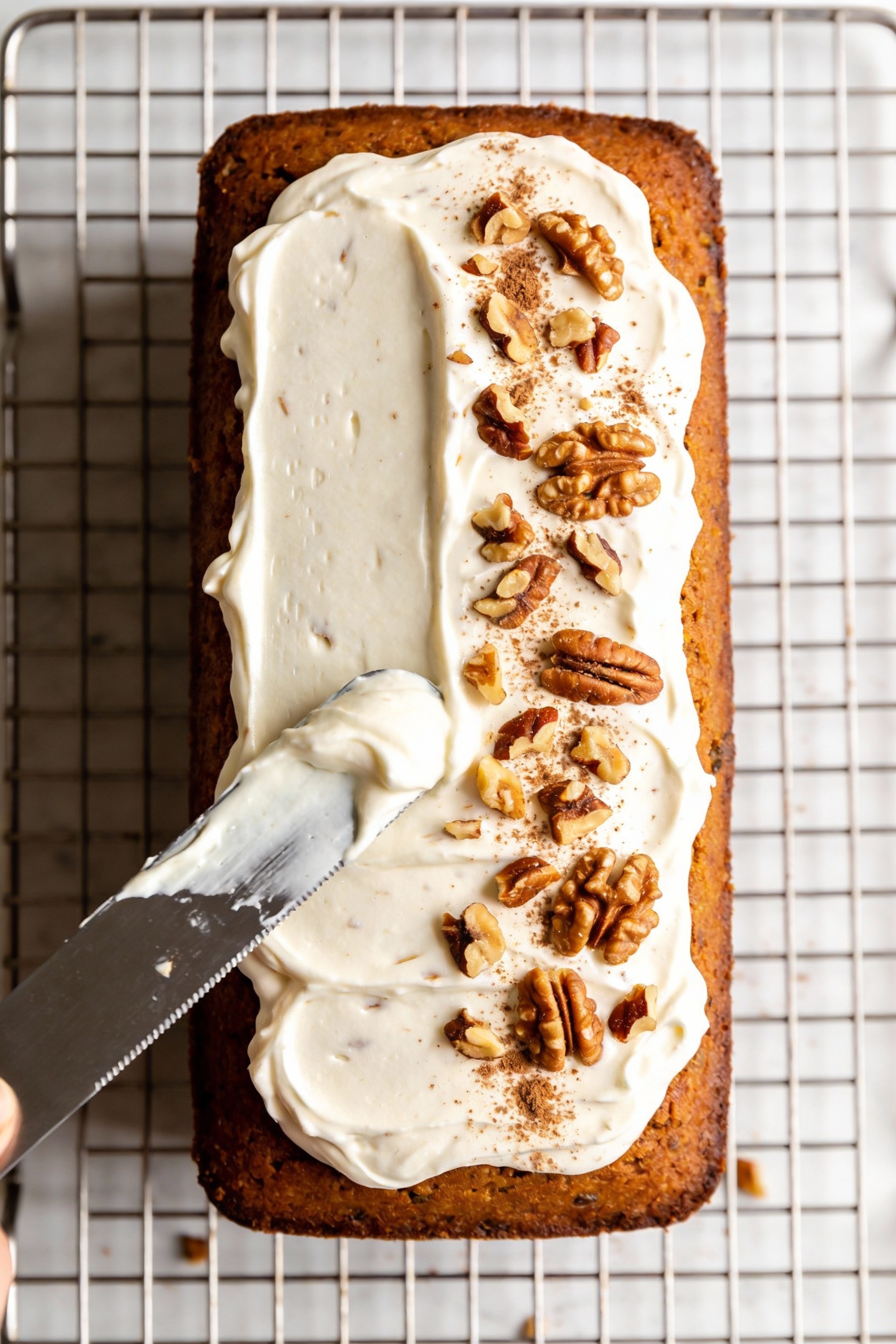 3. Cooking process: Carrot Walnut Spice cake on a wire rack being frosted; offset spatula spreading smooth Greek yogurt–
