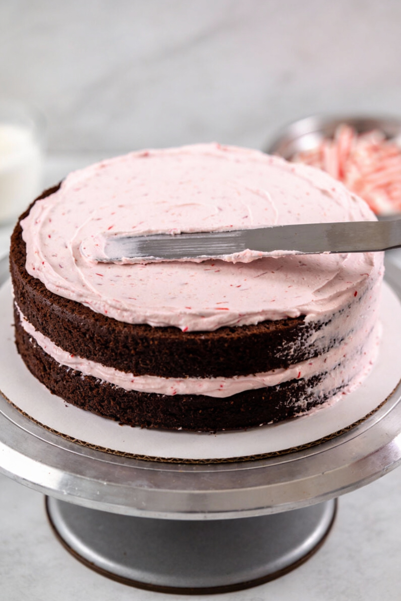 Cooking process shot of chocolate peppermint layer cake being assembled: smooth peppermint buttercream being spread betw