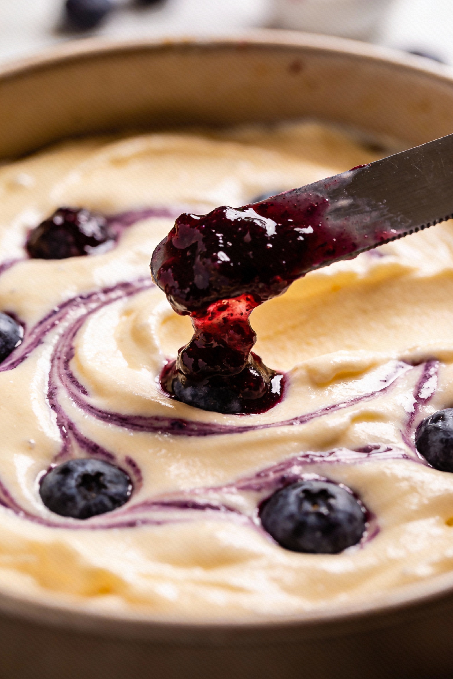 Cooking process: blueberry cake batter in the pan mid-assembly with dollops of jammy mashed blueberry swirl being dragge