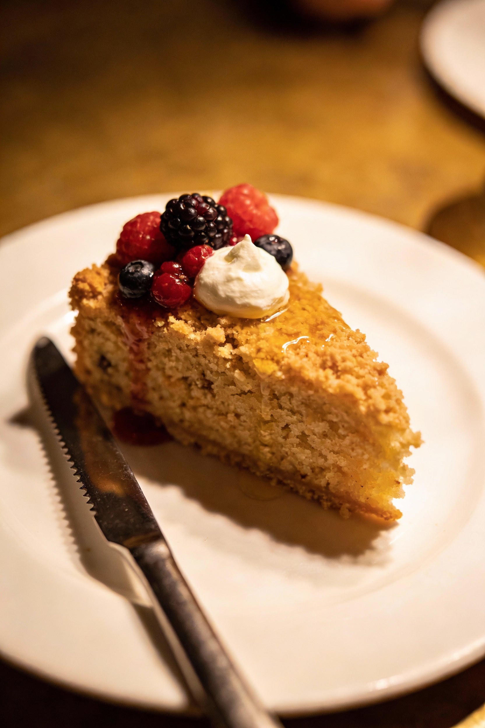 Final plated slice of base cake topped with fresh berries and a small dollop of whipped cream, light glaze sheen on the 