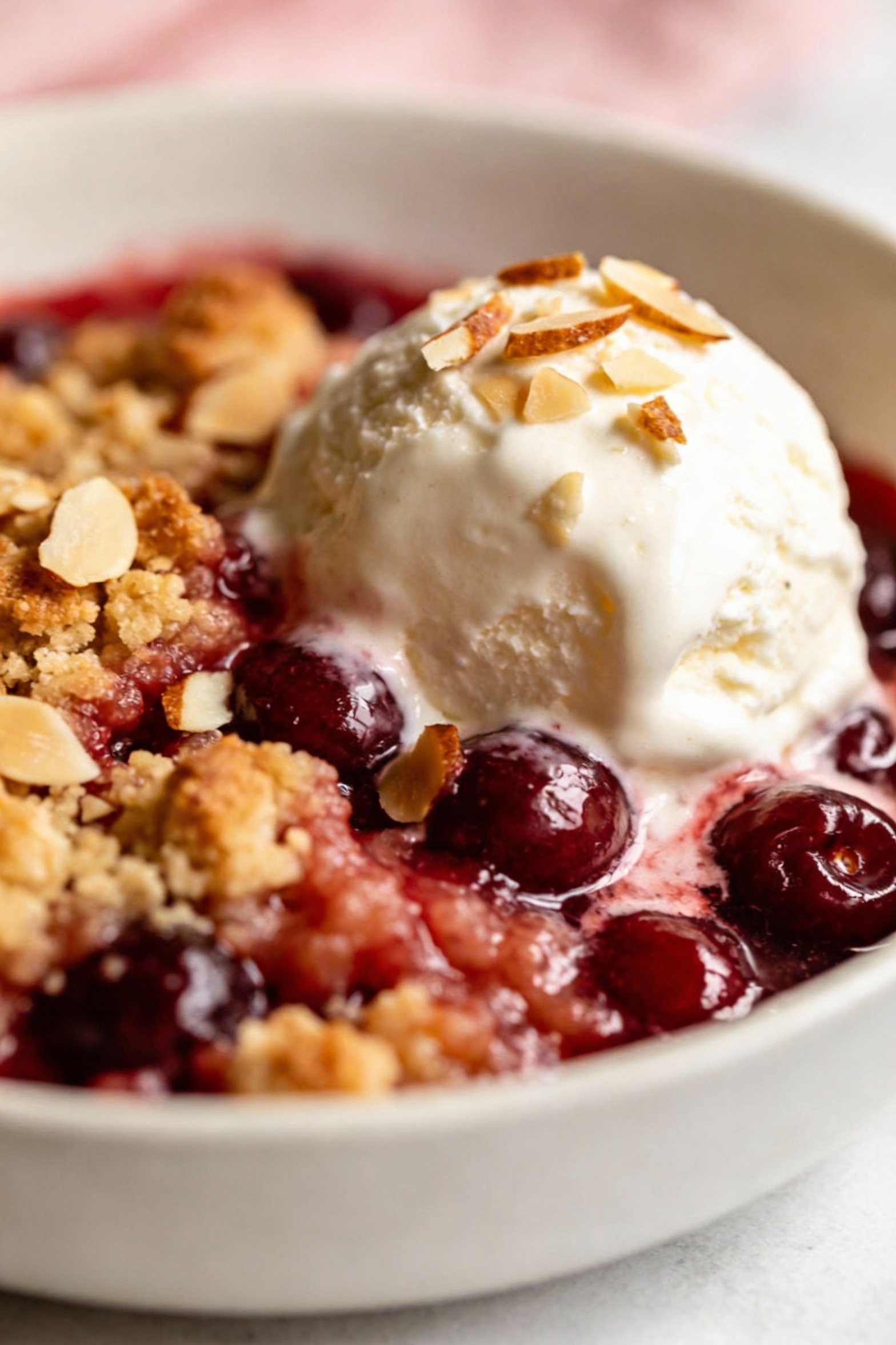 Beautifully plated serving of warm cherry dump cake in a white bowl with a scoop of vanilla ice cream melting into the g
